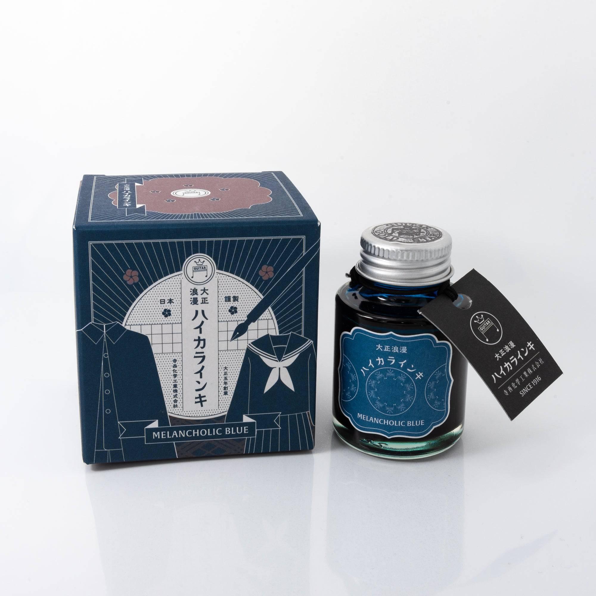 Taisho Romance Melancholic Blue fountain pen ink bottle with a deep blue hue, placed on a wooden desk under soft natural light.