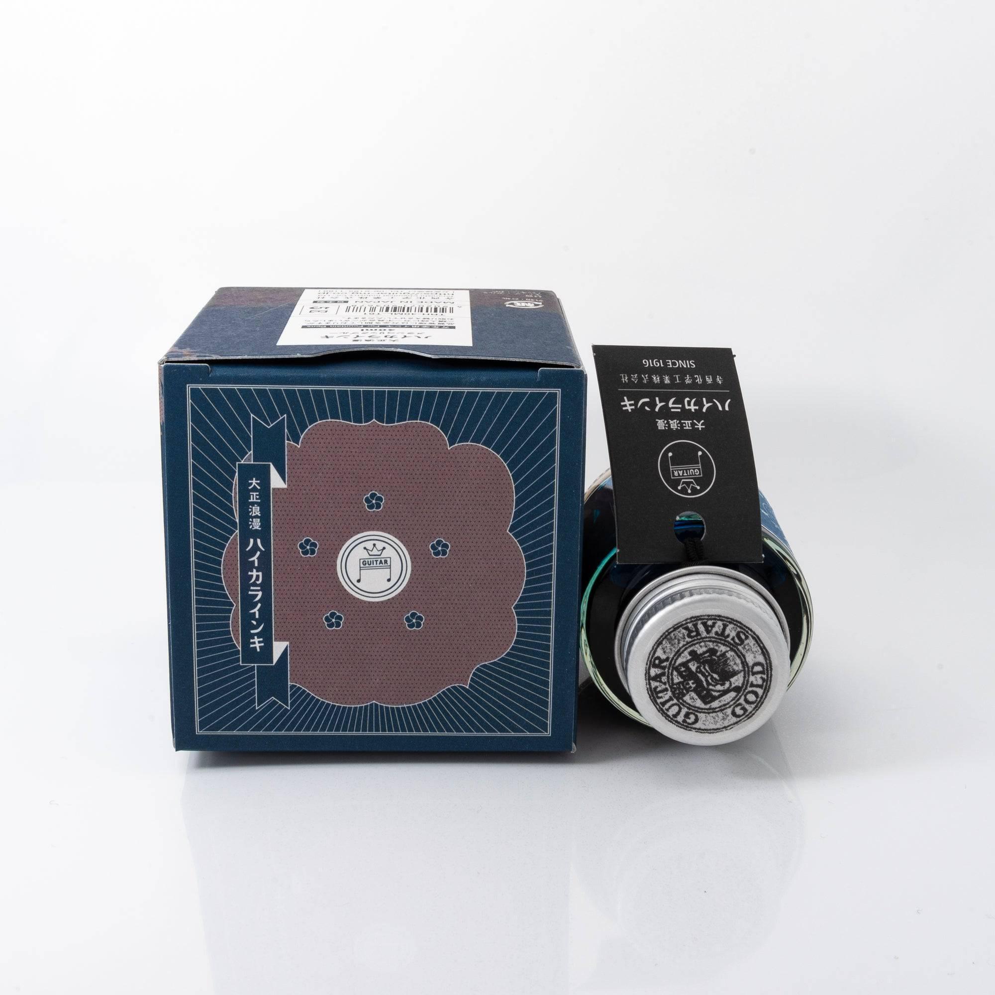 Taisho Romance Melancholic Blue fountain pen ink bottle and matching pen, arranged on a wooden desk, emphasizing classic design.