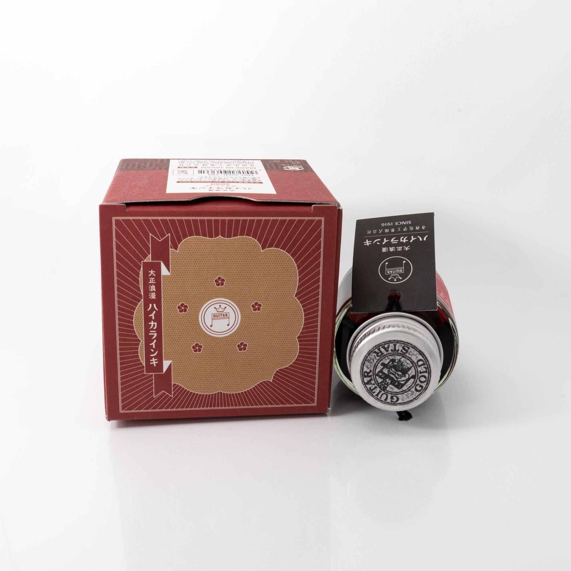 Taisho Romance Modern Red fountain pen ink bottle and matching pen, arranged on a wooden desk, emphasizing a classic design.