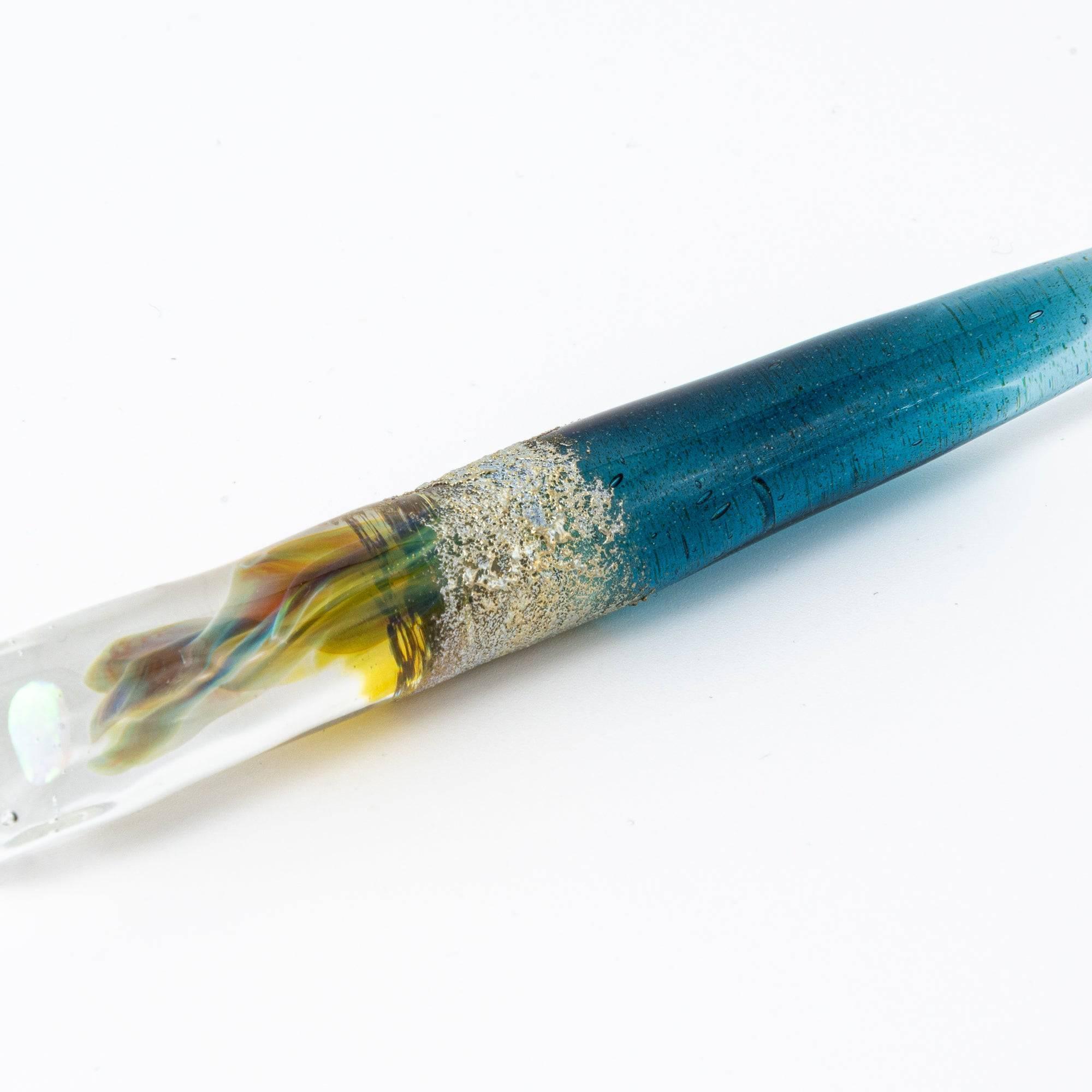 Ethereal deep blue glass dip pen with smooth transparent barrel and twisted glass nib in profile view with holder