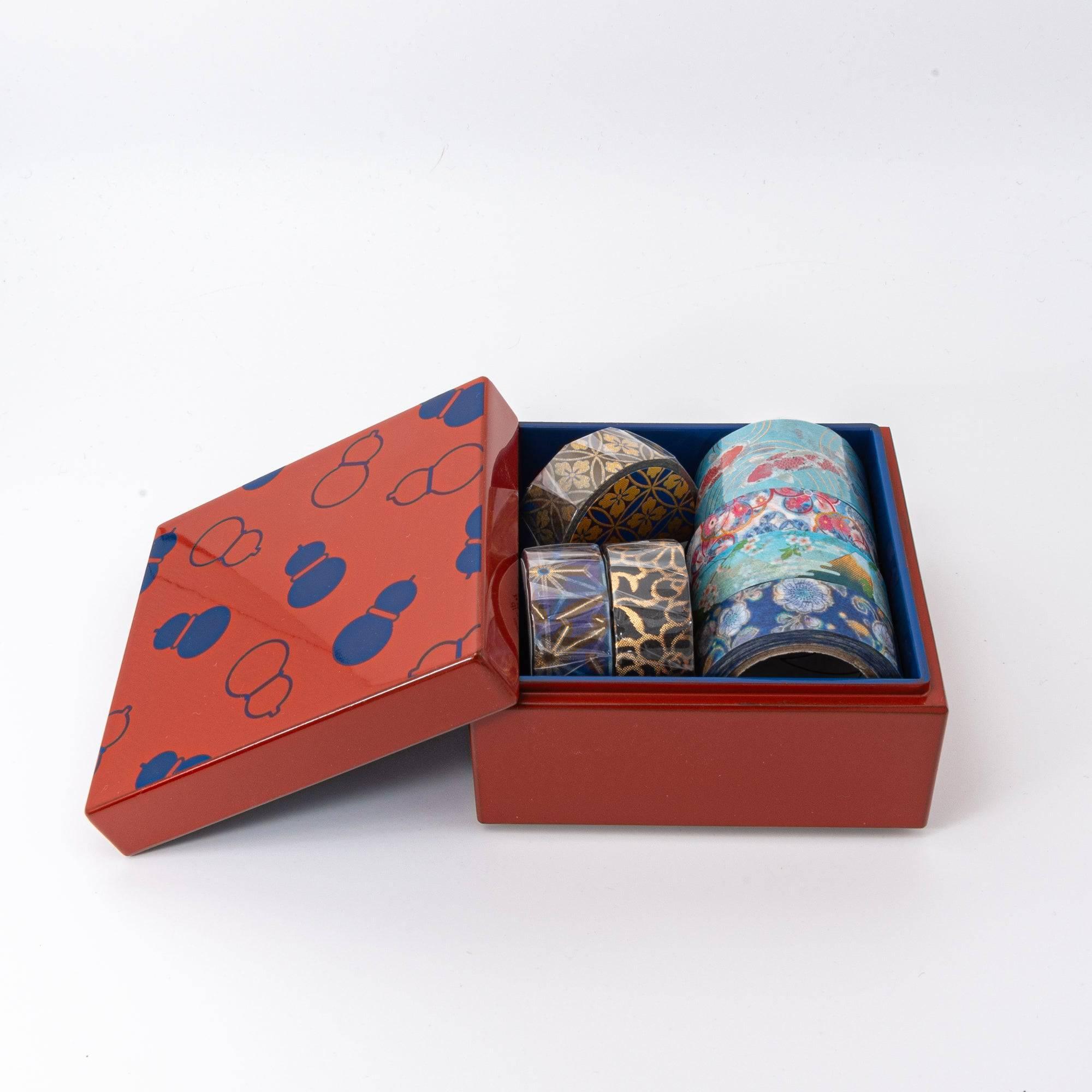 Open red Japanese lacquer stationery box with blue gourd patterns and a blue interior, holding multiple colorful washi tape rolls, displayed on a white background.