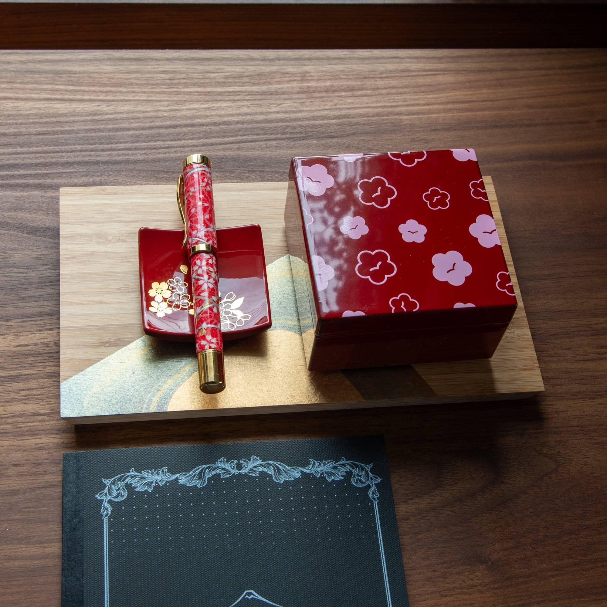 Urushi kohako plum lacquer trinket box lifestyle photograph with matching red patterned pen on wooden base