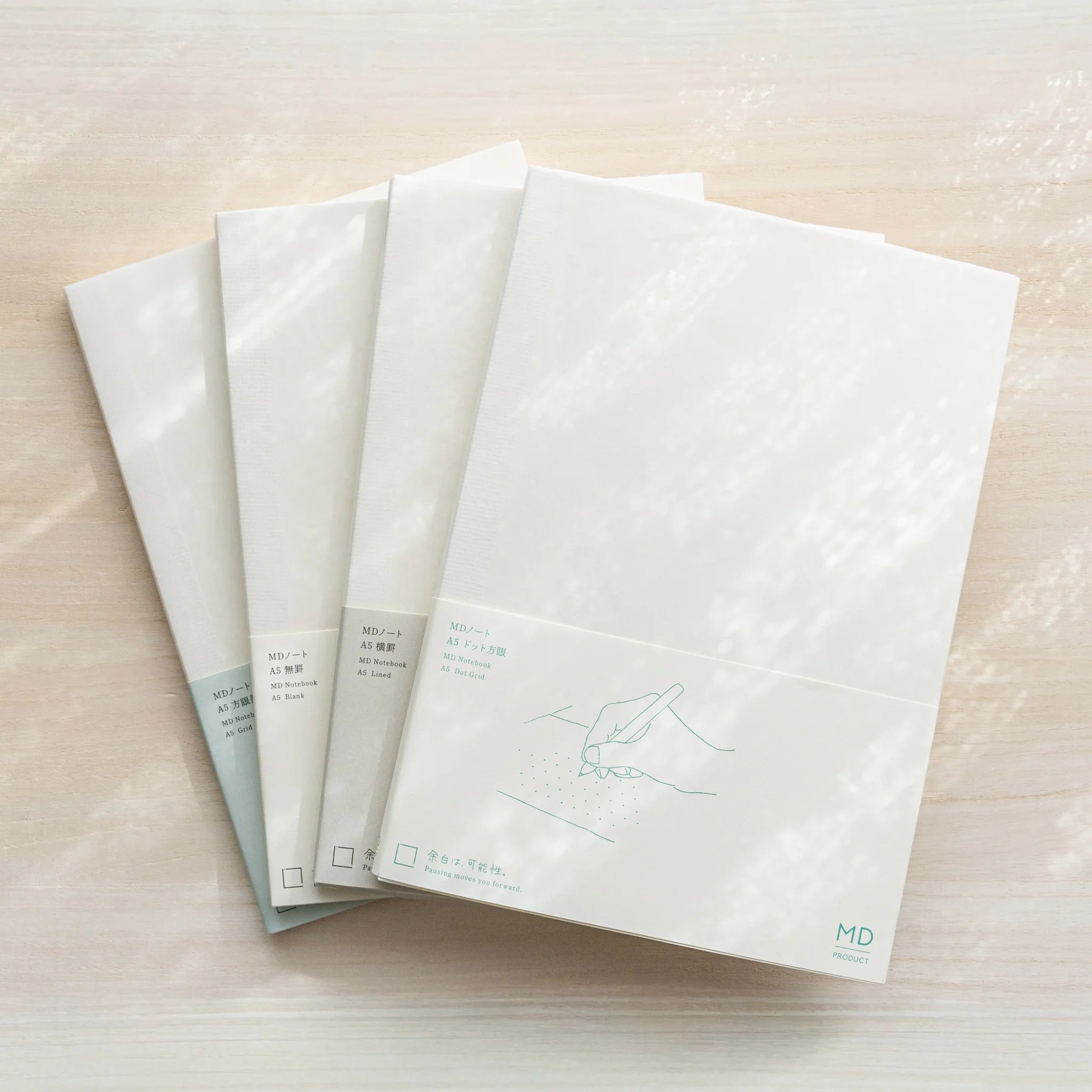 Four Midori MD A5 Japanese notebooks in glassine wrapping with belly bands, fanned out showing different page variants