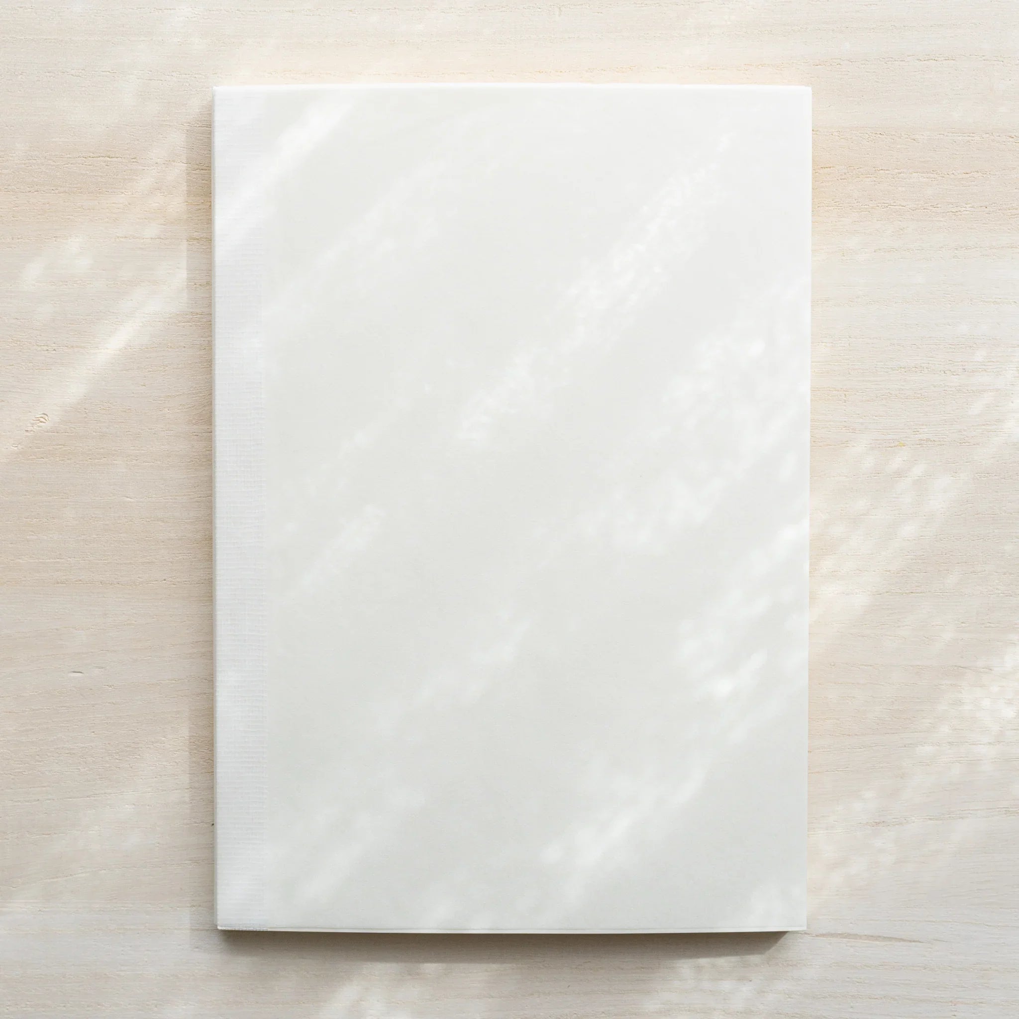Midori MD Notebook A5 in glassine wrapping without belly band, white cover with woven texture visible on light wood