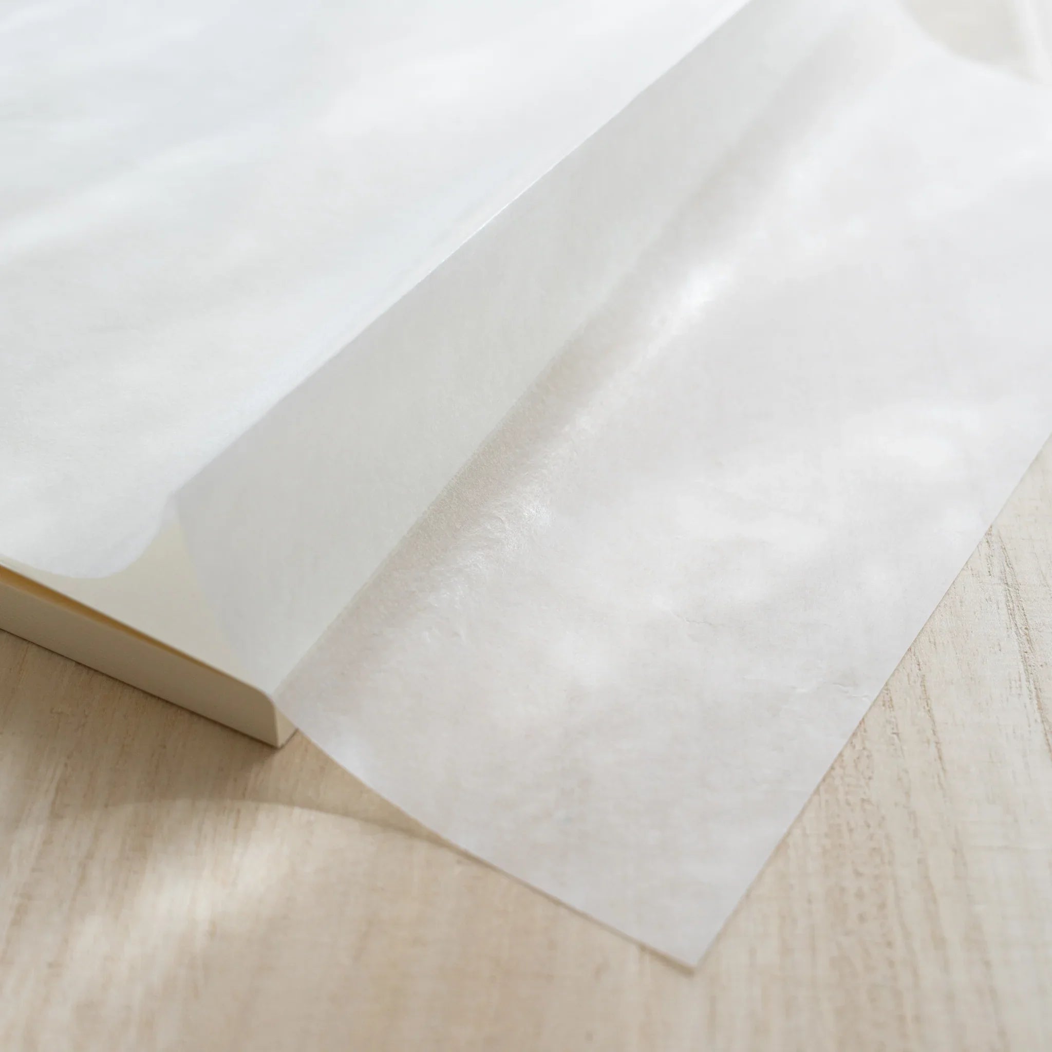Translucent glassine wrapping paper peeled back from Midori MD Notebook A5, revealing white linen-textured cover underneath