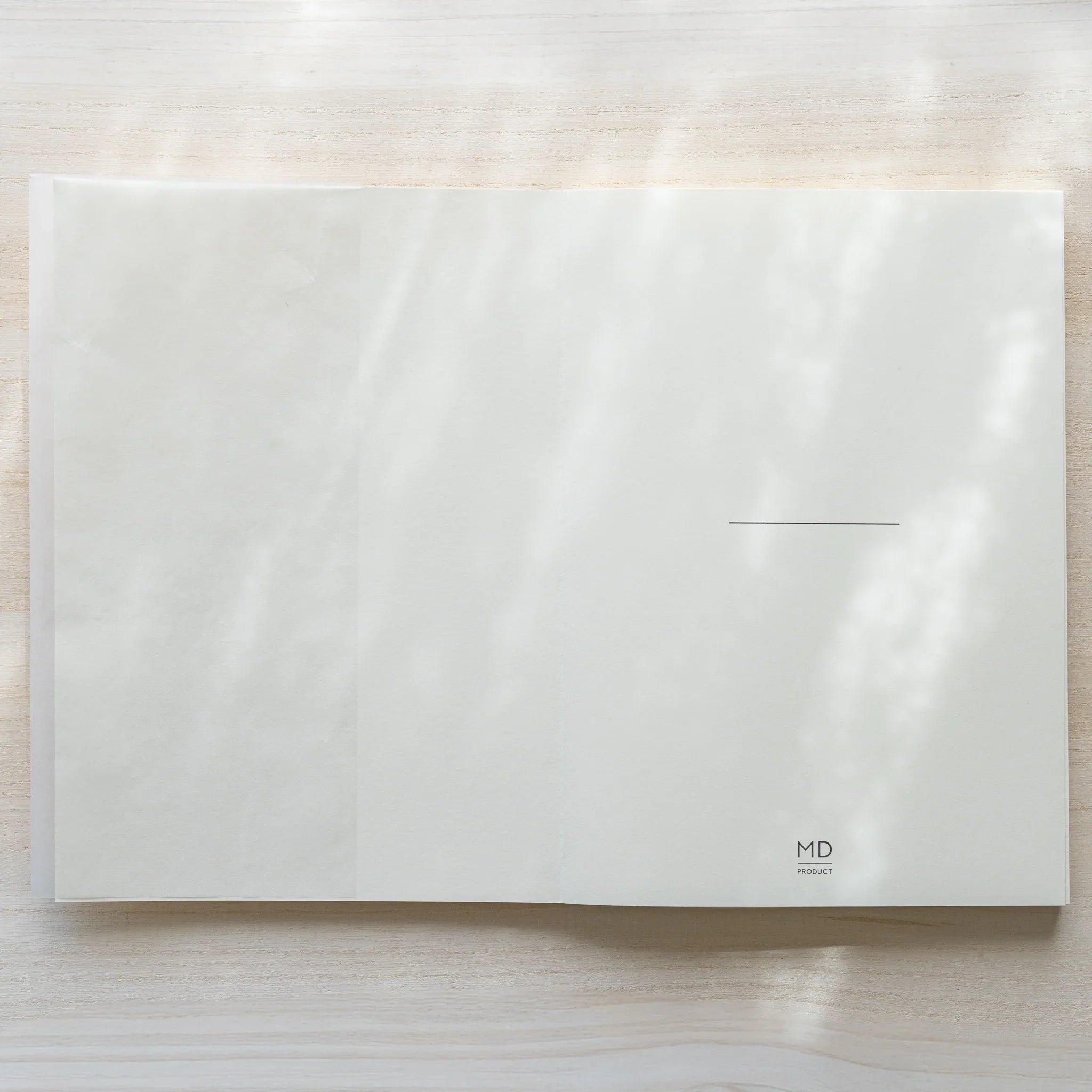 Midori MD Notebook A5 in glassine wrapping lying flat horizontally, showing back cover with MD Product logo and center line