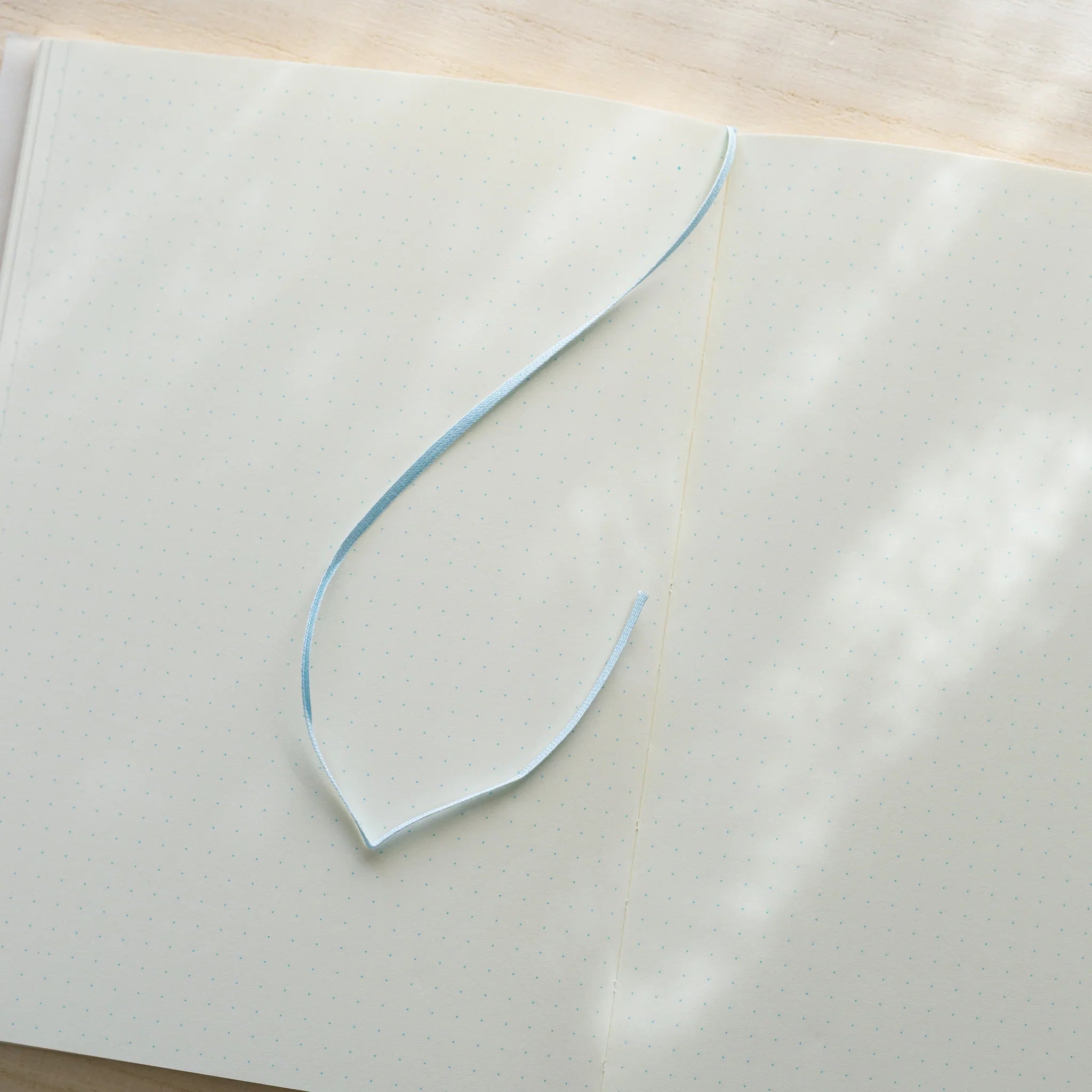Midori MD Notebook A5 open to ivory dot grid spread, light blue satin ribbon bookmark curled on left page