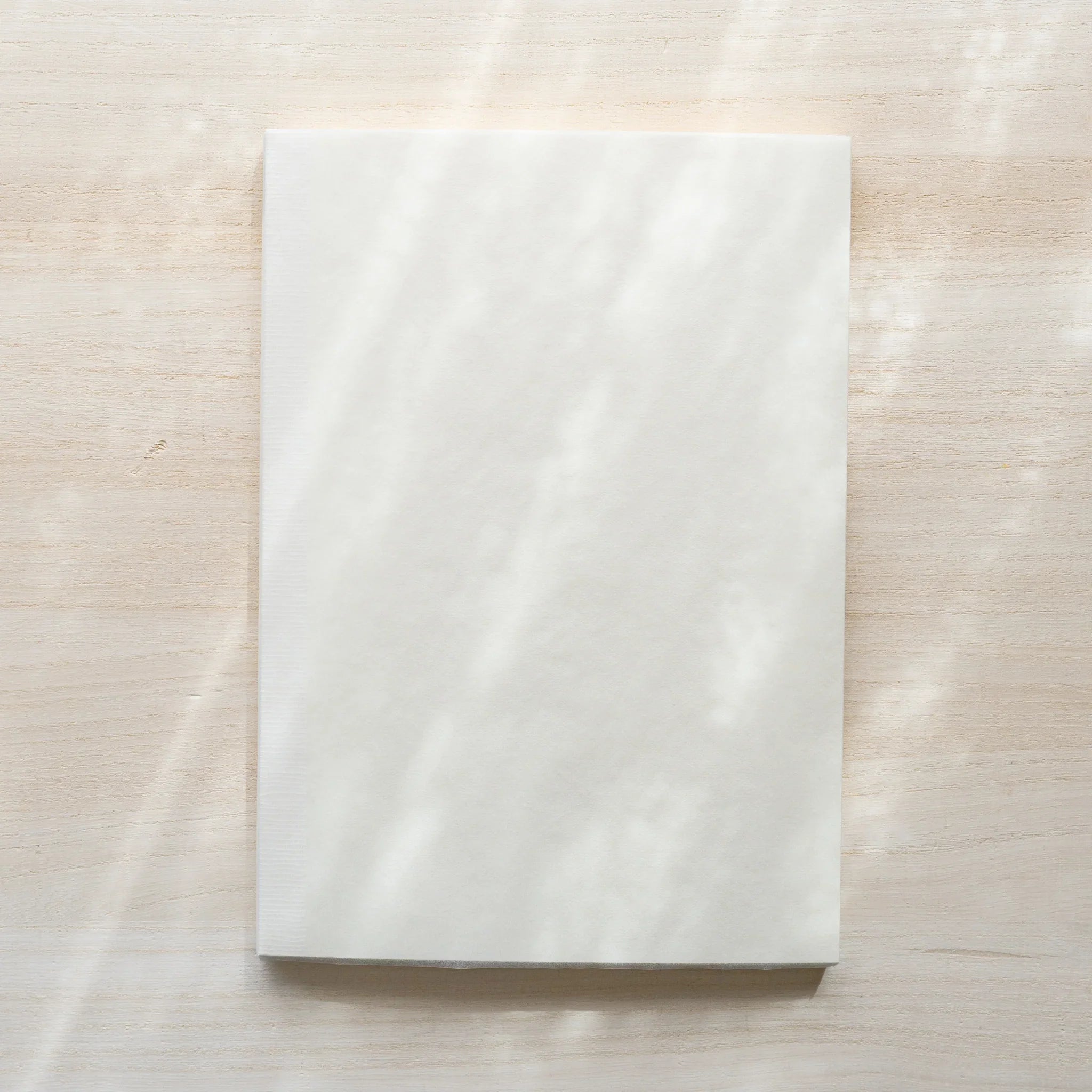 Midori MD Notebook A5 in glassine wrapping, front view showing white translucent cover on wood surface, no belly band