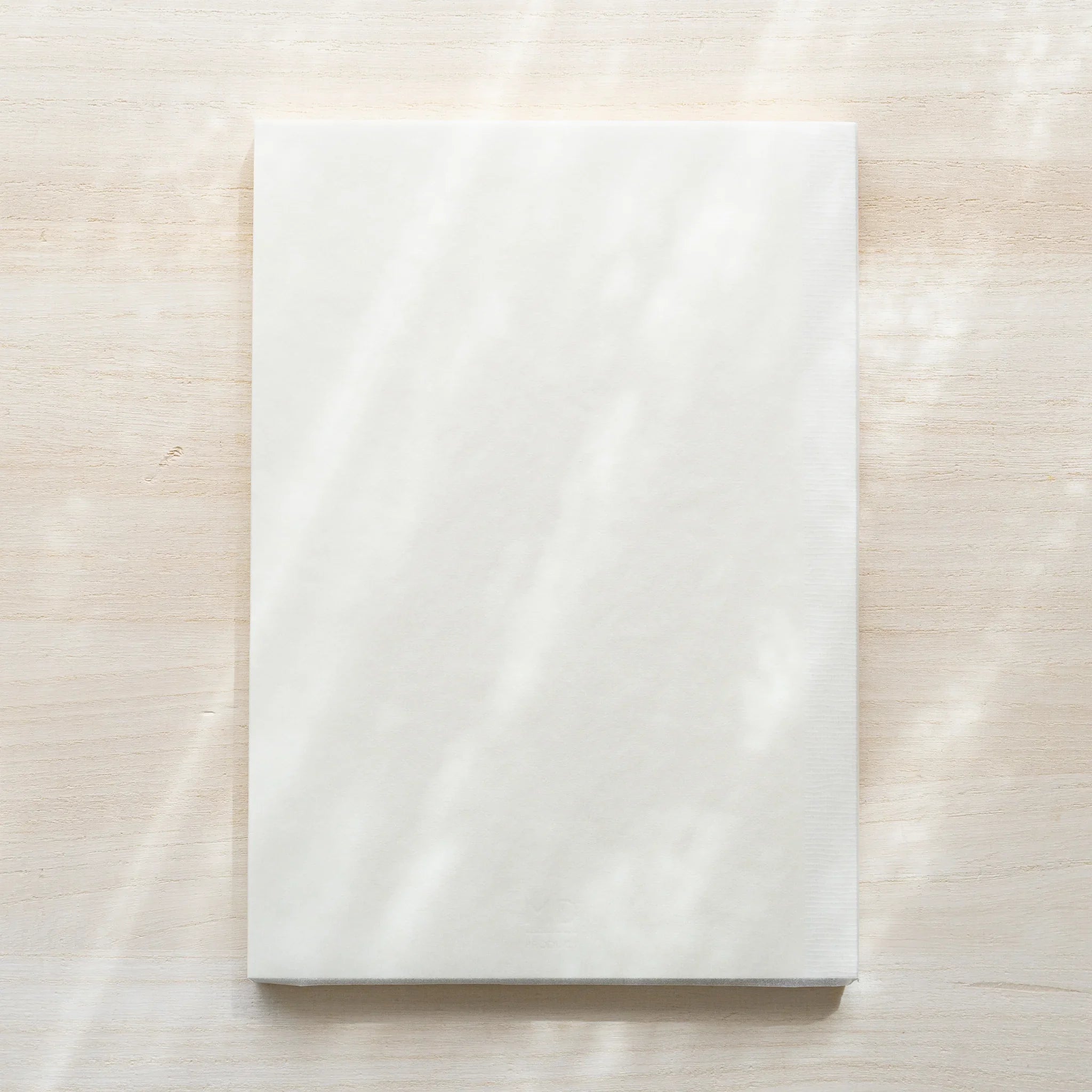 Midori MD Notebook A5 Lined in glassine wrapping, front view showing white translucent cover on wood surface, no belly band