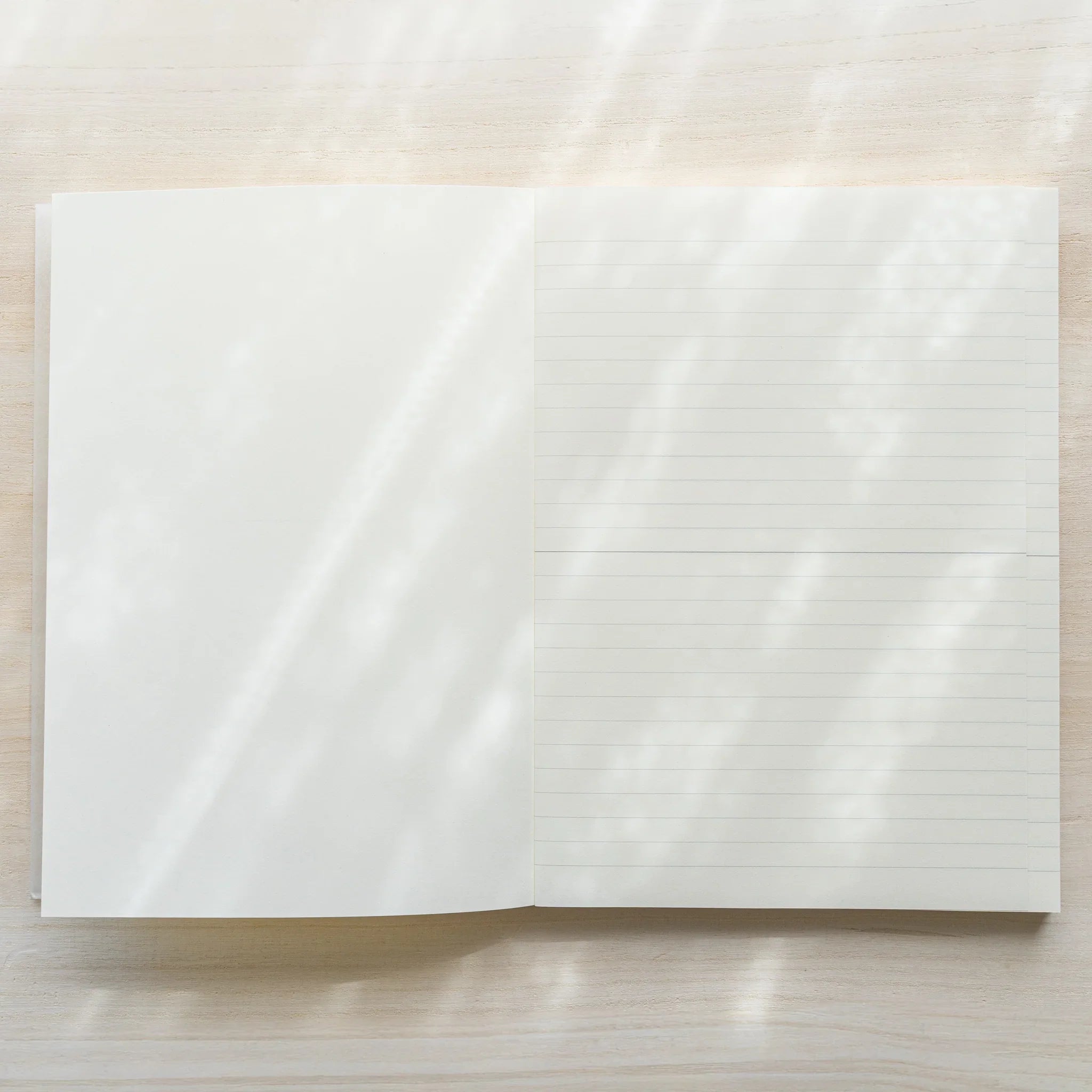 Midori MD Notebook A5 opened flat from above, left page blank white, right page showing lined ruling, center spine on wood