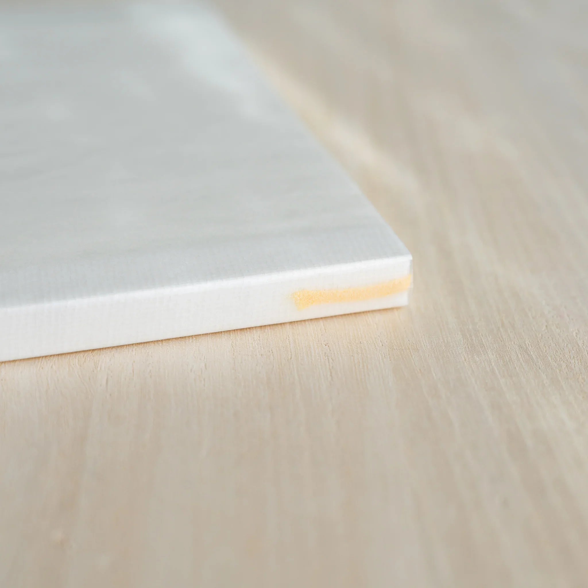 Closed Midori MD Notebook A5, angled view showing white linen cover, ivory page edges, and yellow ribbon bookmark at corner