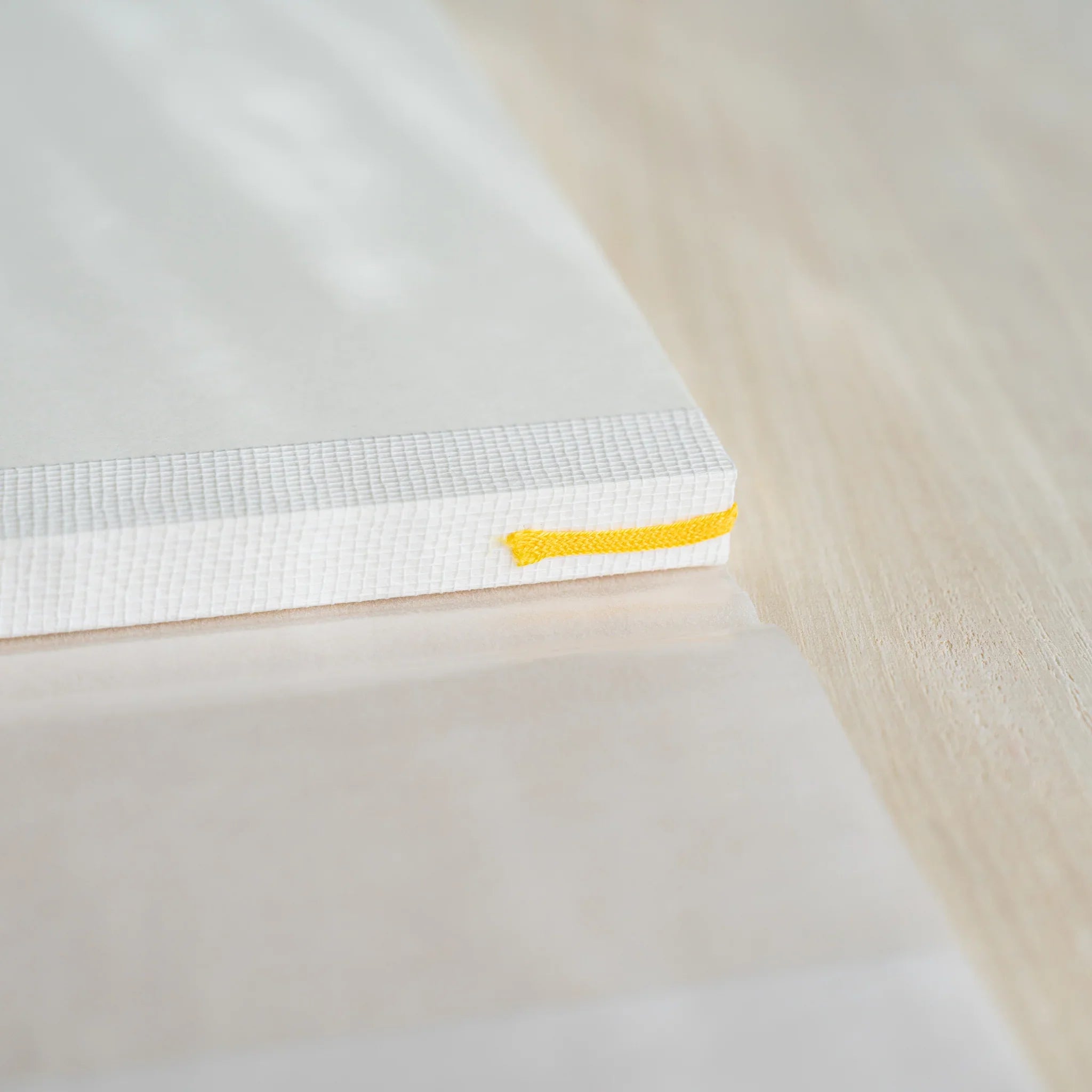 Close-up of Midori MD Notebook A5 spine corner showing ivory page stack, thread-stitched binding, and yellow satin ribbon
