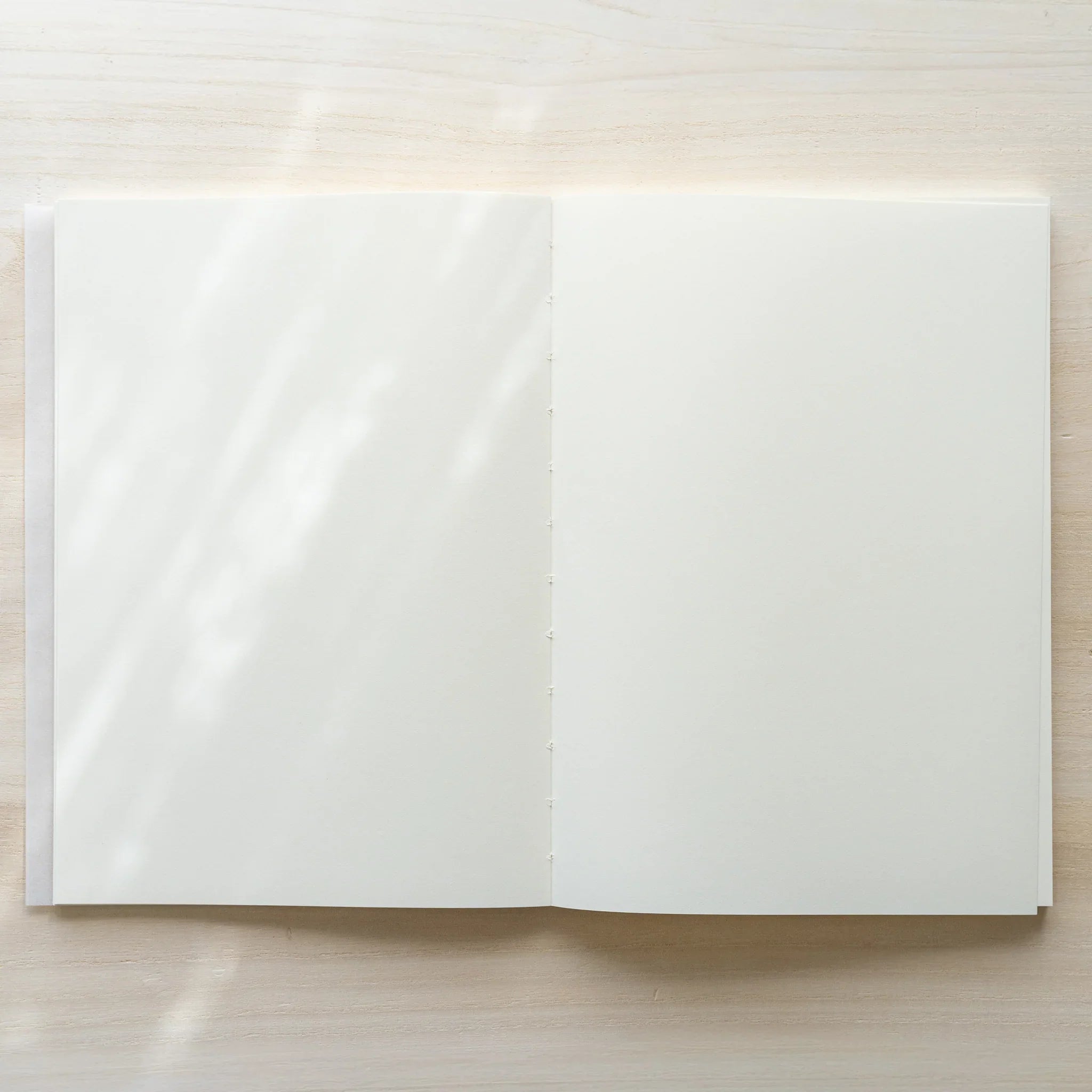 Midori MD Notebook A5 opened flat from above showing two blank white pages and center thread-stitched spine on wood surface