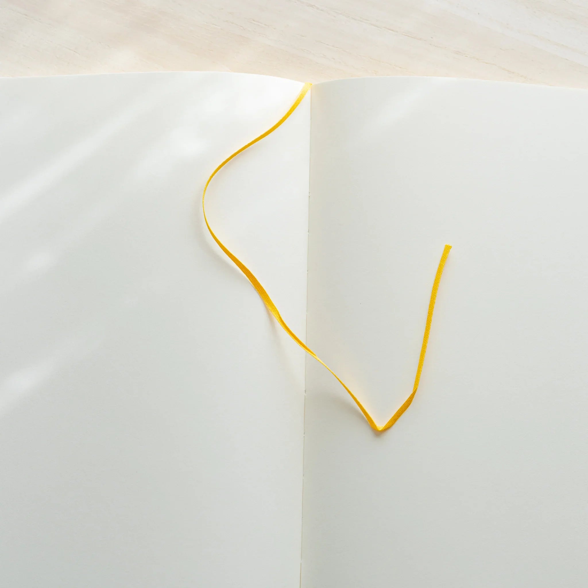 Midori MD Notebook A5 open to blank ivory spread, yellow satin ribbon bookmark curled on left page, center spine visible