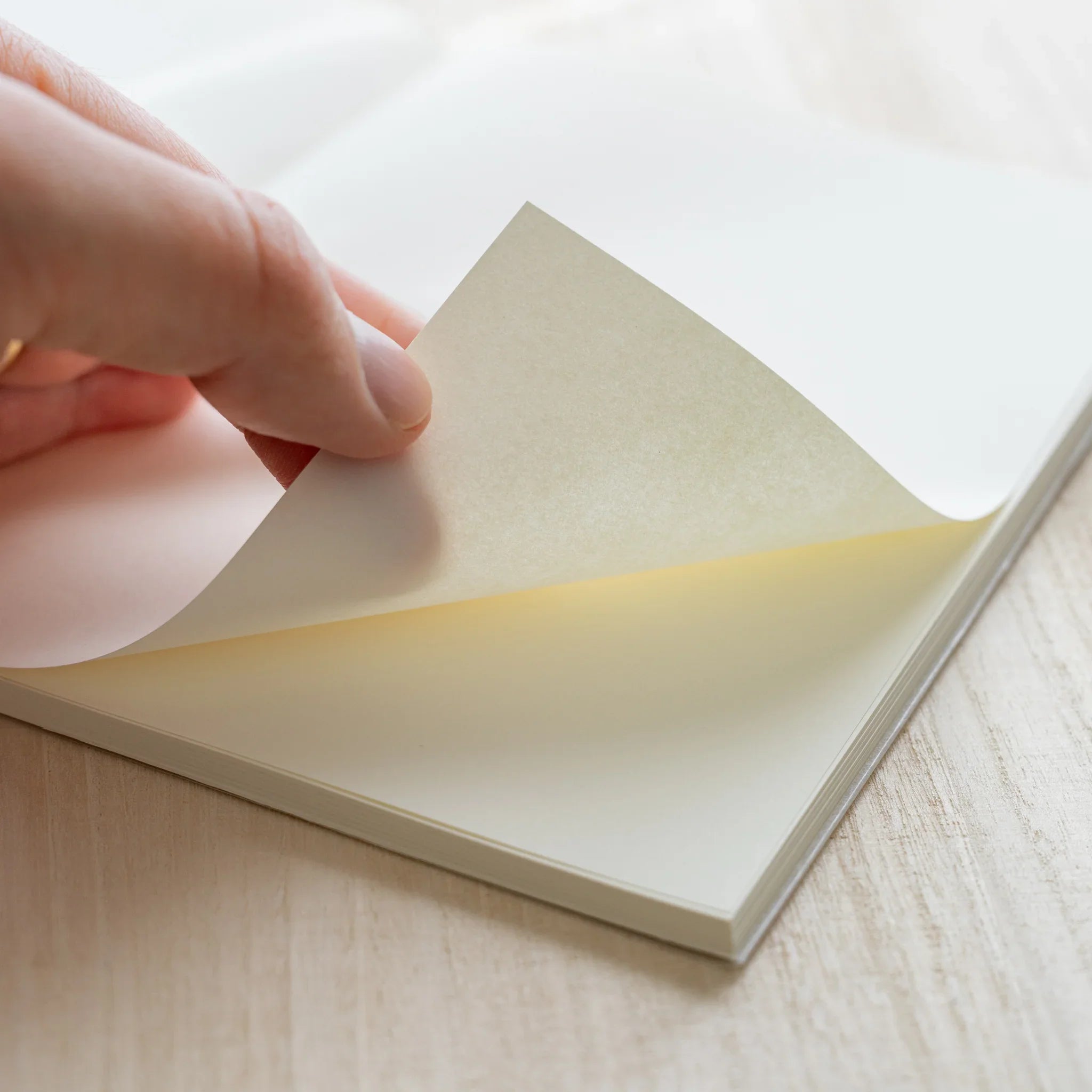 Hand turning blank ivory page of Midori MD Notebook A5, showing warm ivory paper tone and page thickness on wood surface