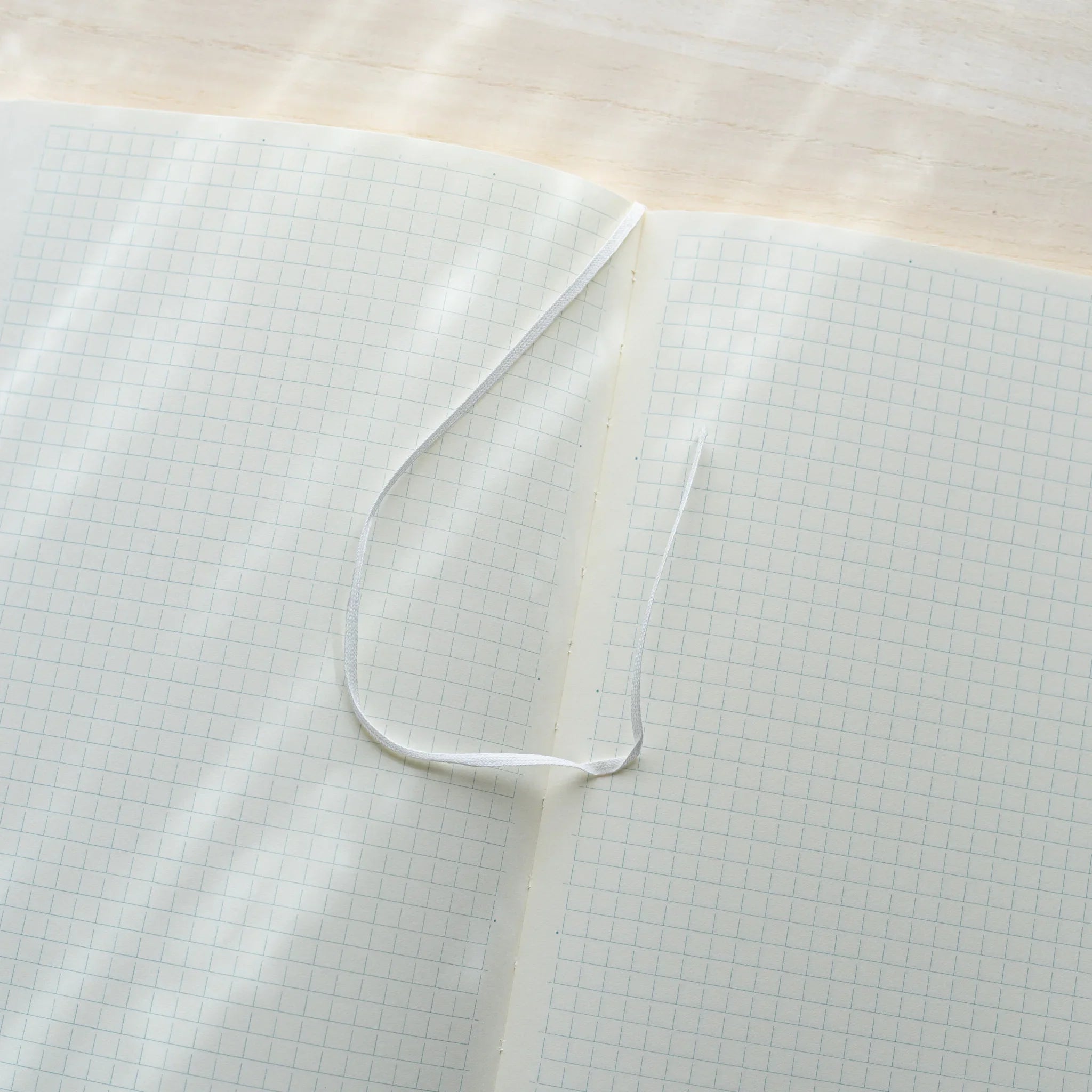 Midori MD Notebook A5 opened to ivory grid spread, white satin ribbon bookmark curled on left page, center spine visible