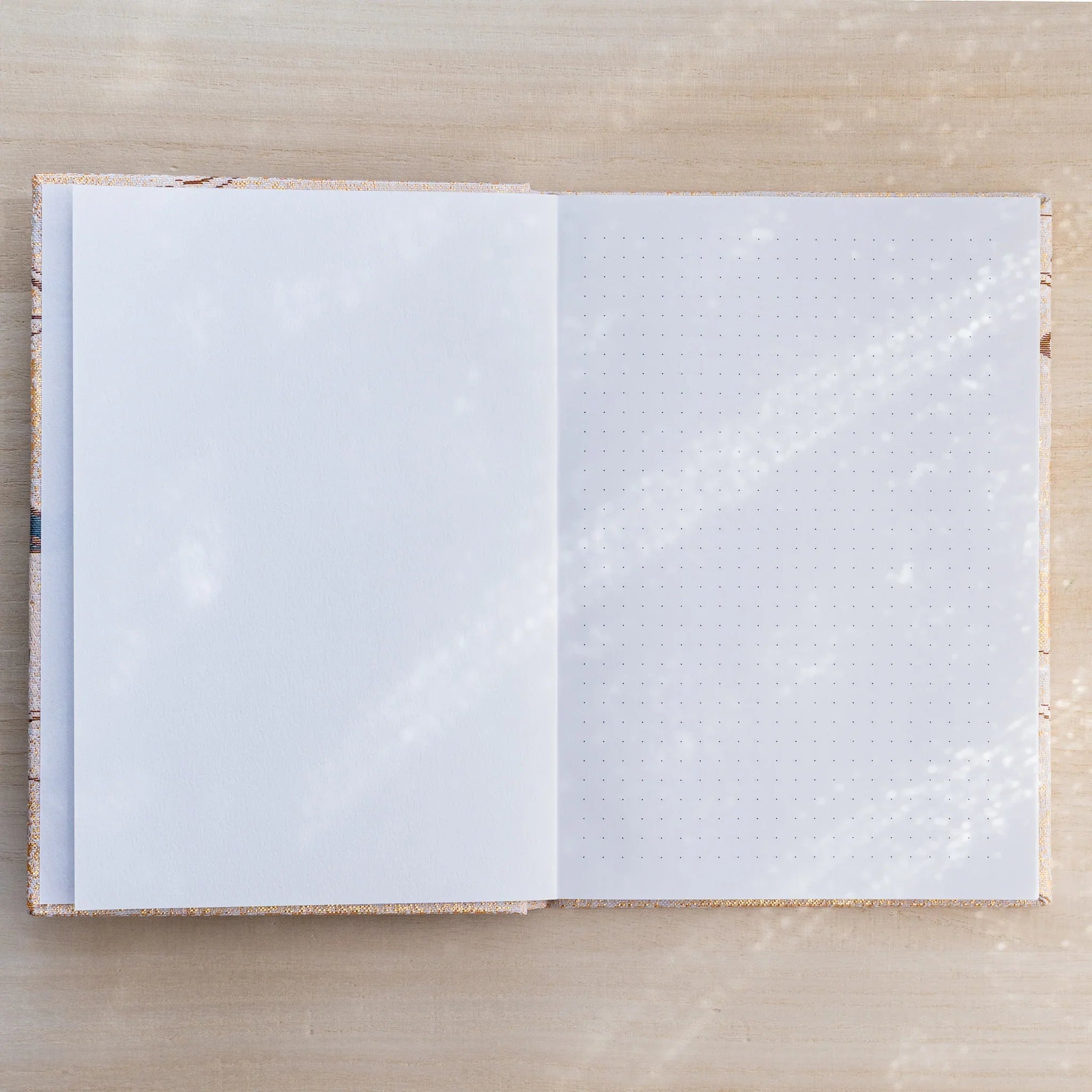 Notebook open showing a blank white page on left and a dot grid page on right, gold textile cover edges