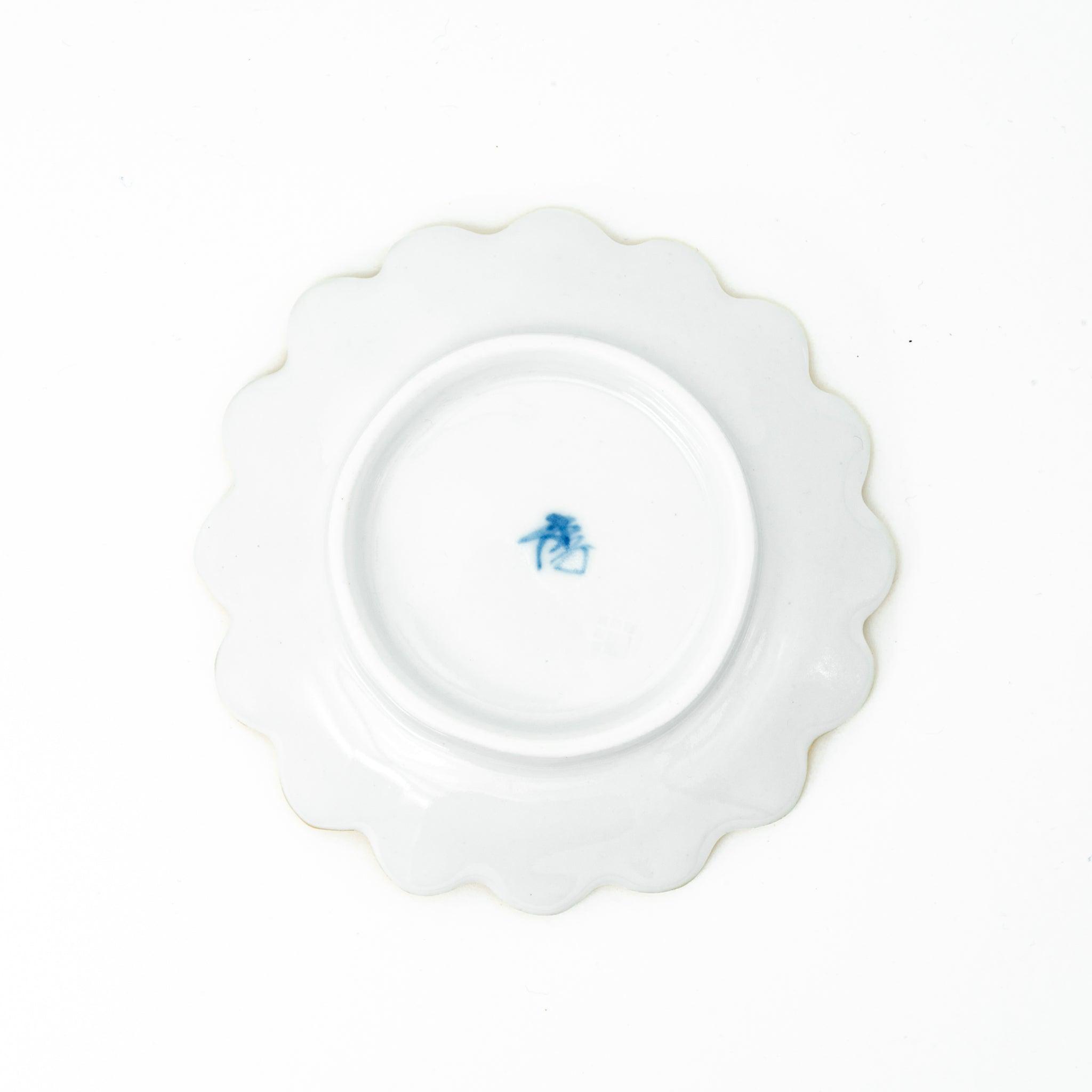 The underside of a scalloped gold ceramic dish, featuring a blue maker’s mark, ideal for Japanese stationery.  