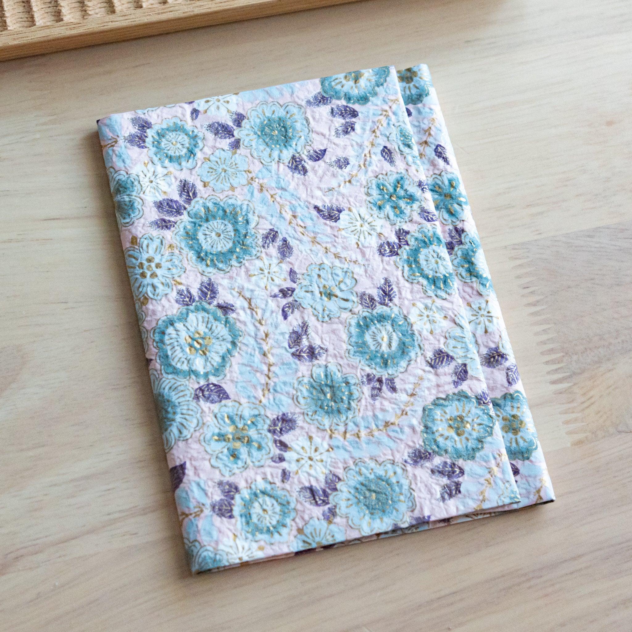 Floral-patterned notebook with textured cover closed and placed on a light wooden surface.