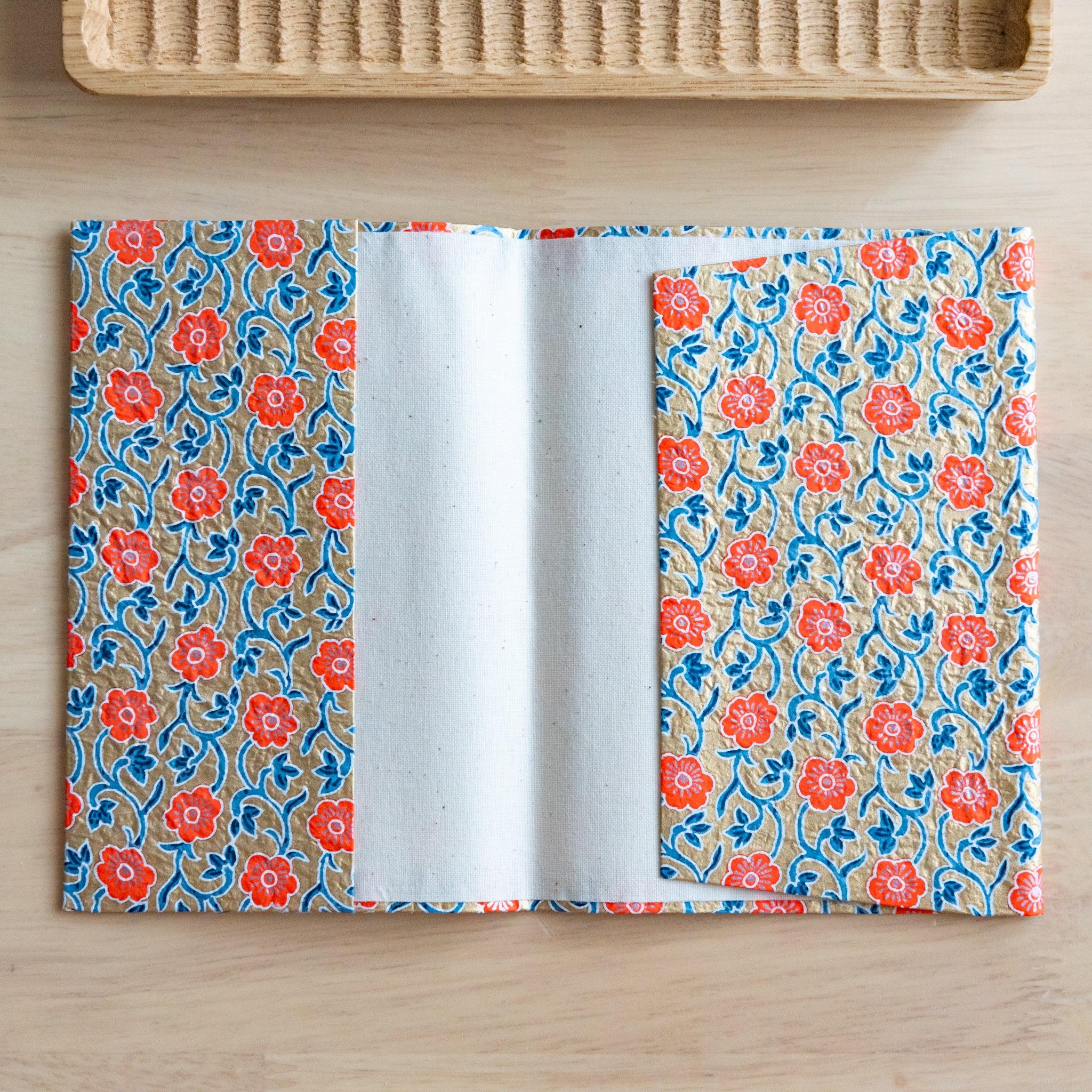 Open notebook with a floral-patterned fabric cover showing its inner lining, placed on a light wooden surface.