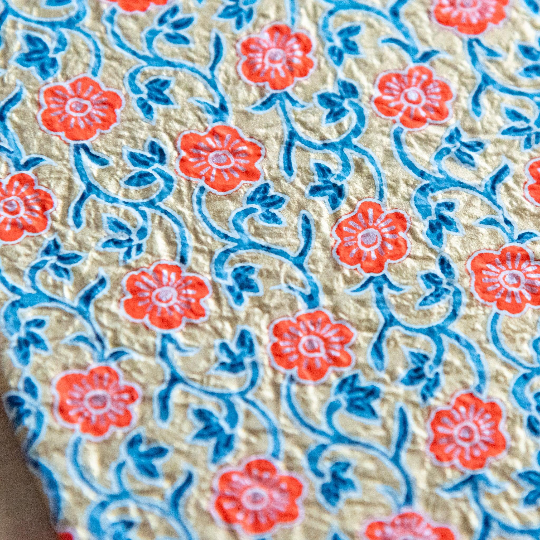 Close-up of a textured floral notebook cover with orange flowers and blue vines on a beige background.