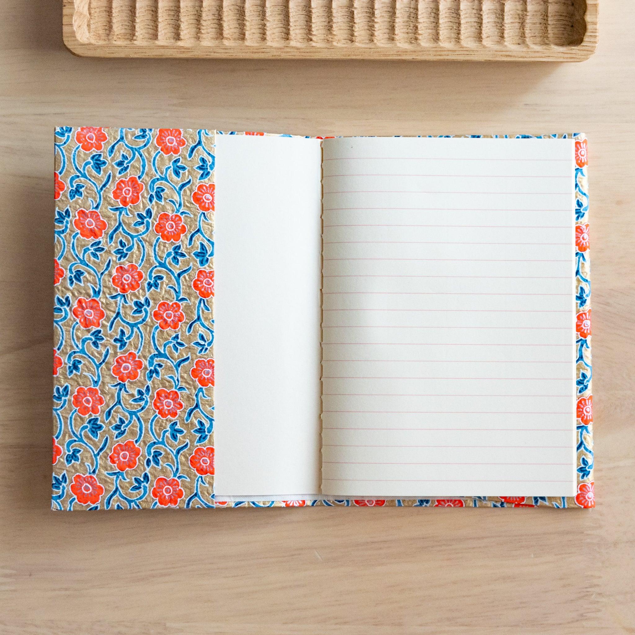 Open notebook with floral-patterned cover and lined pages, placed on a wooden surface near a rattan tray.