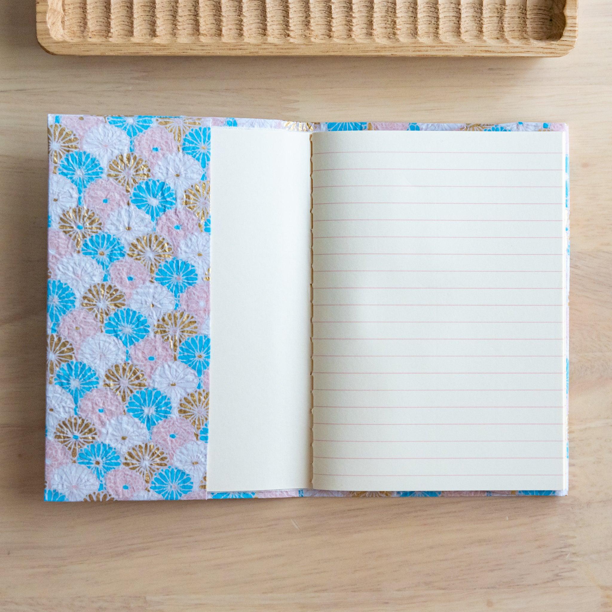 Open notebook with pastel pink and blue patterned fabric cover and lined pages, placed on a wooden surface.