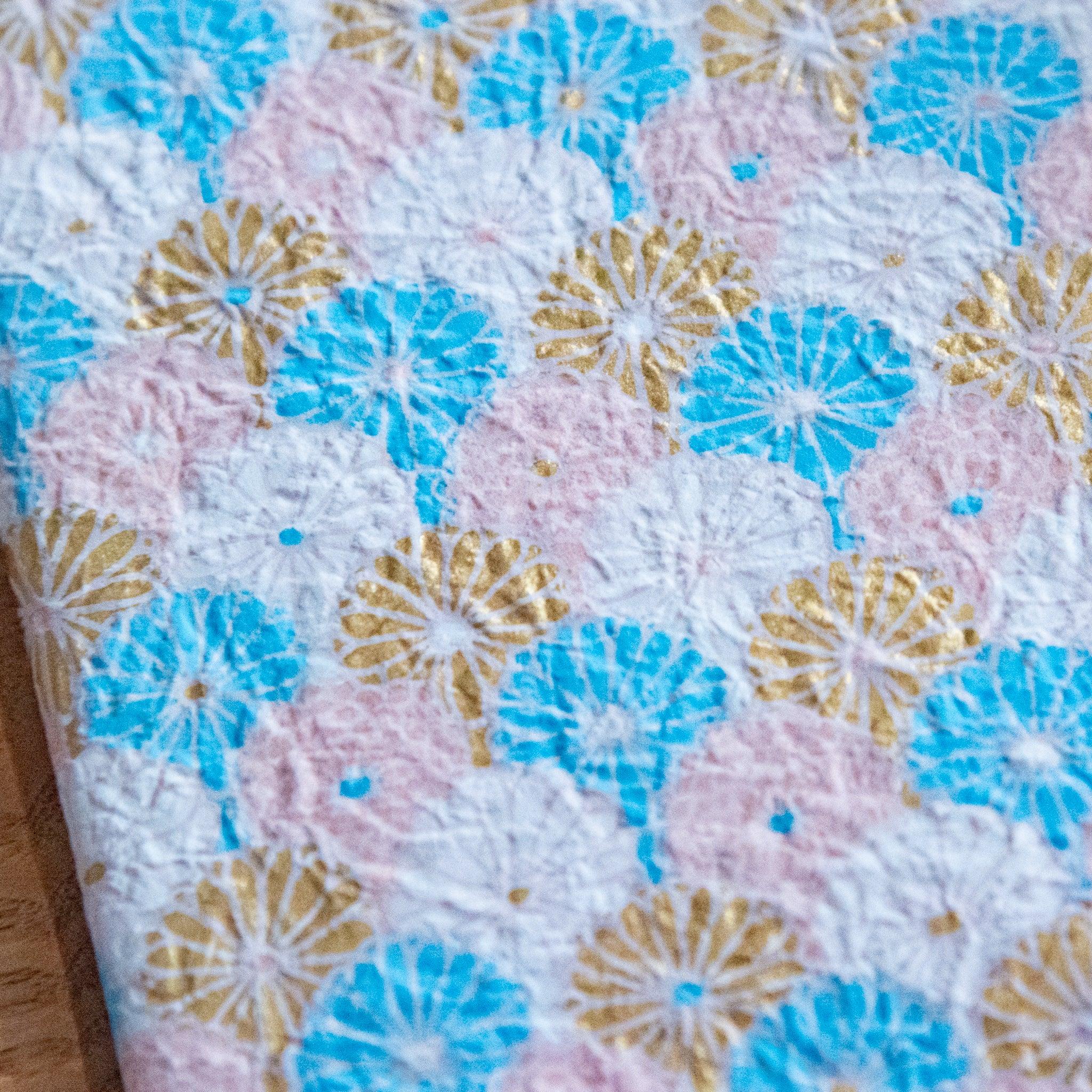 Close-up of a notebook cover featuring textured blue, gold, and pastel pink fan-shaped patterns.