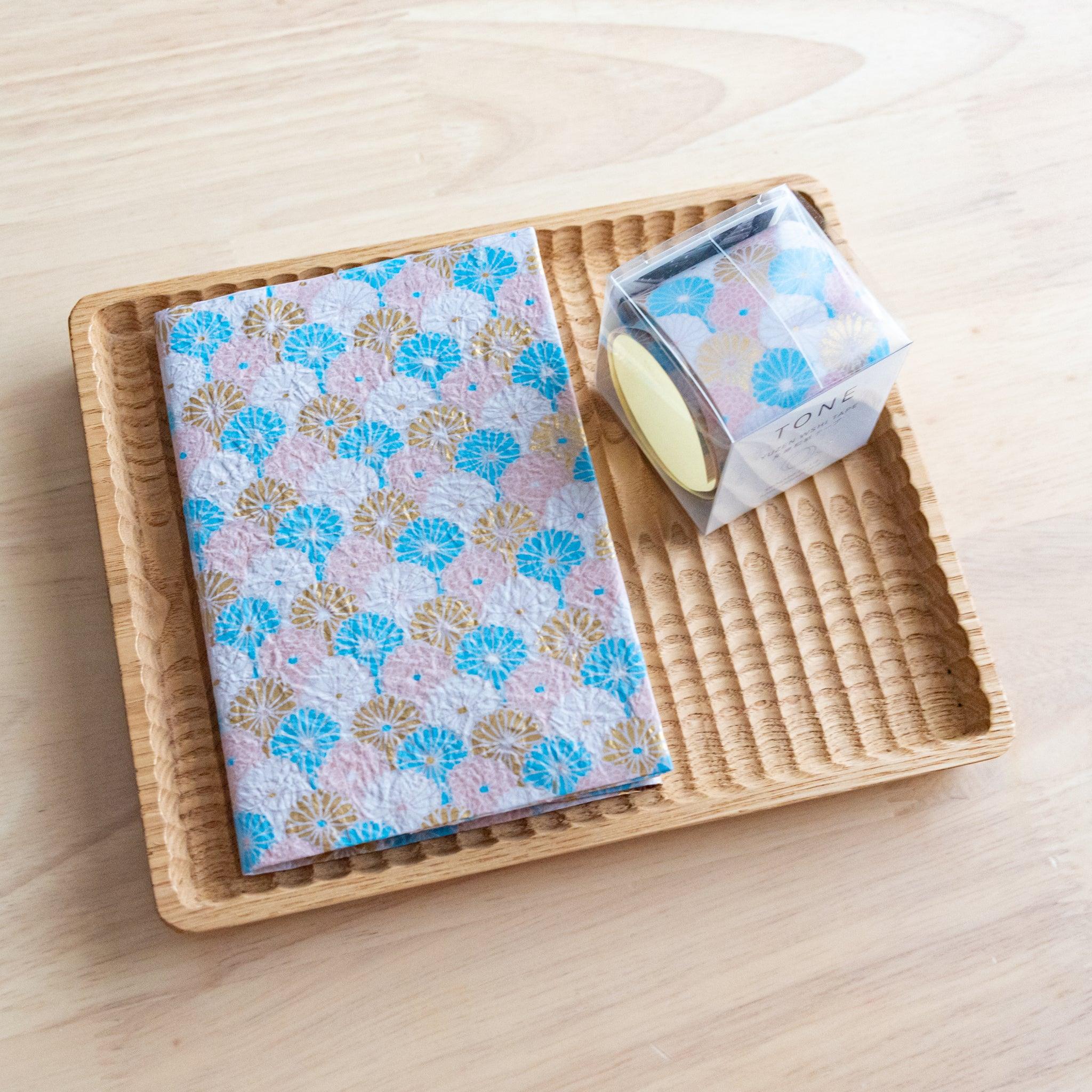 Notebook with blue and gold patterned cover placed in a rattan tray alongside a matching decorative tape.