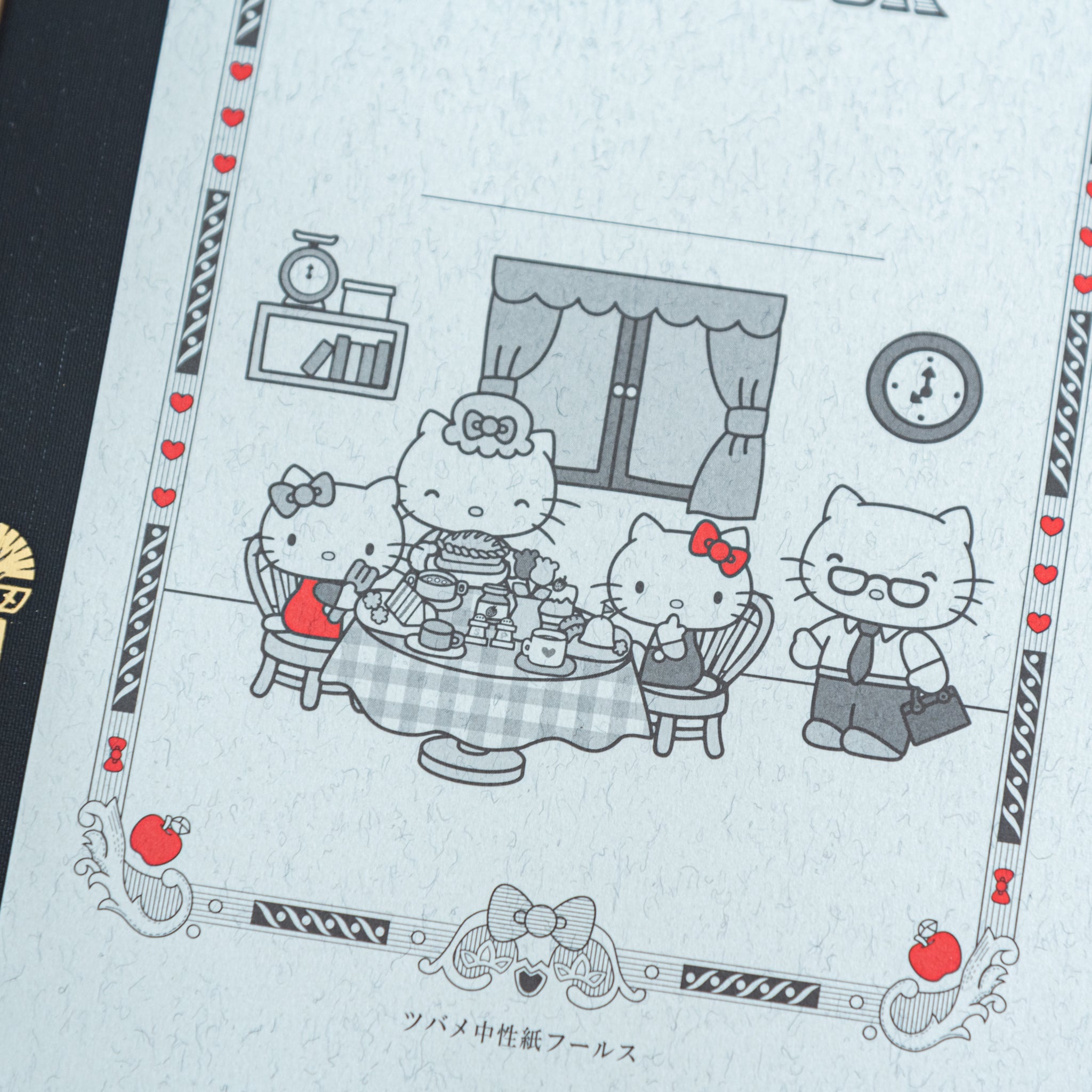 A detailed view of the Tsubame Japanese notebook’s Hello Kitty illustration, depicting a family tea party with red accents, combining elegance with playful Japanese stationery.  