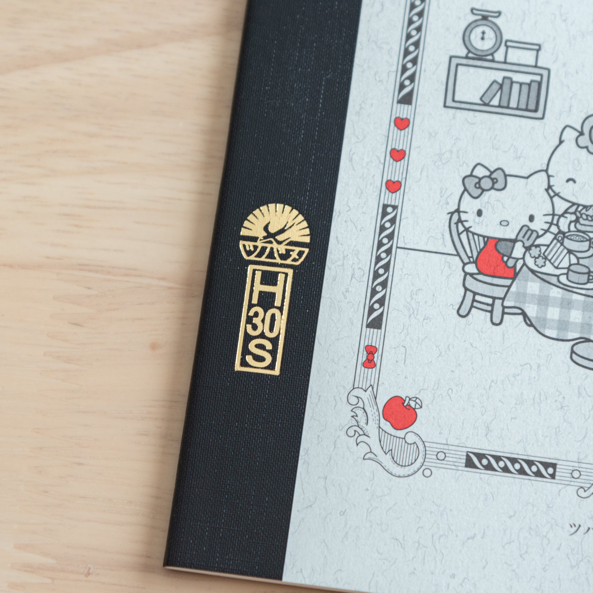 A close-up of a Tsubame Japanese notebook’s spine, featuring a gold-stamped logo and part of the Hello Kitty design with red accents, highlighting premium Japanese stationery.  