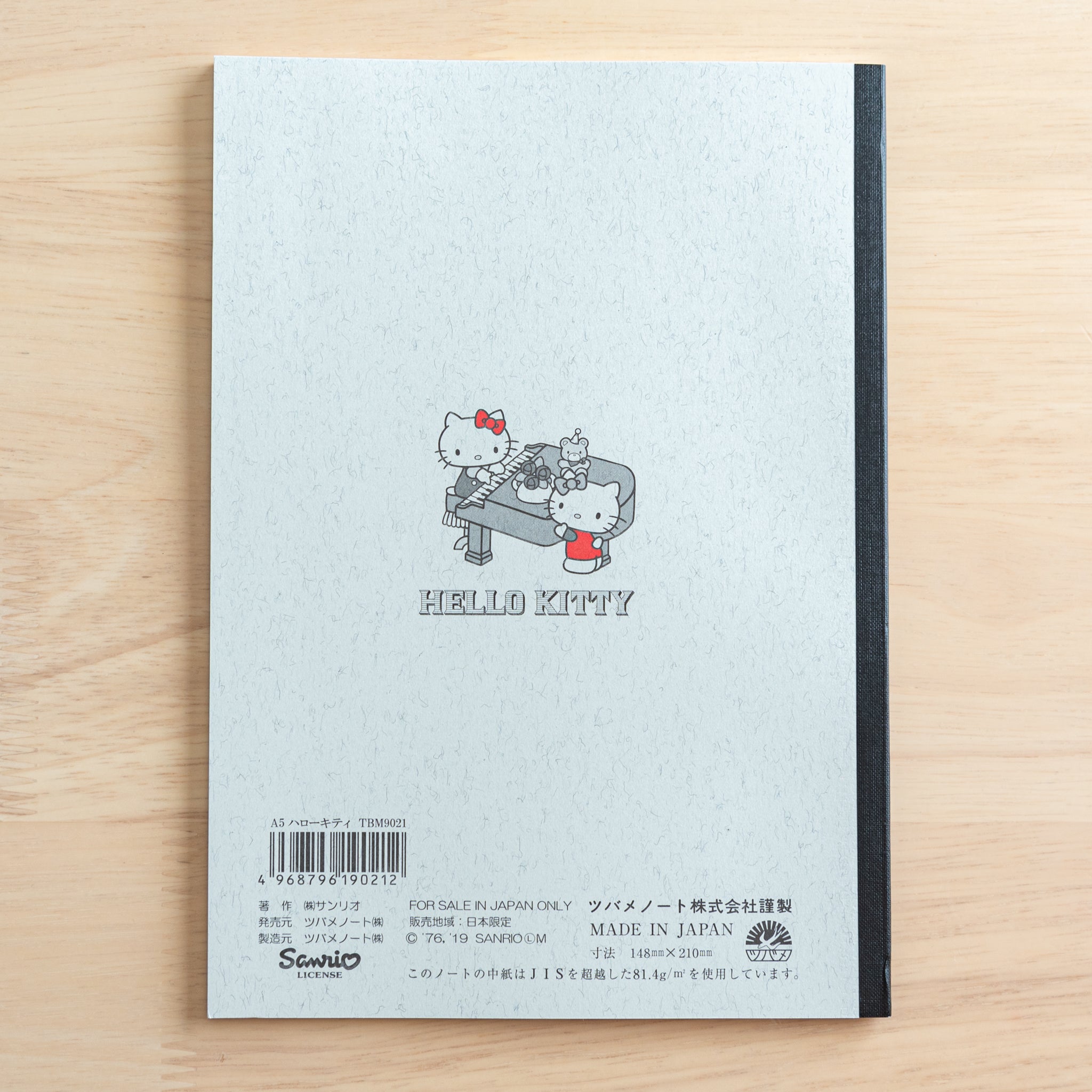 The back cover of a Tsubame Japanese notebook with a Hello Kitty design, featuring a piano illustration, a black spine, product details, and a "Made in Japan" label.  