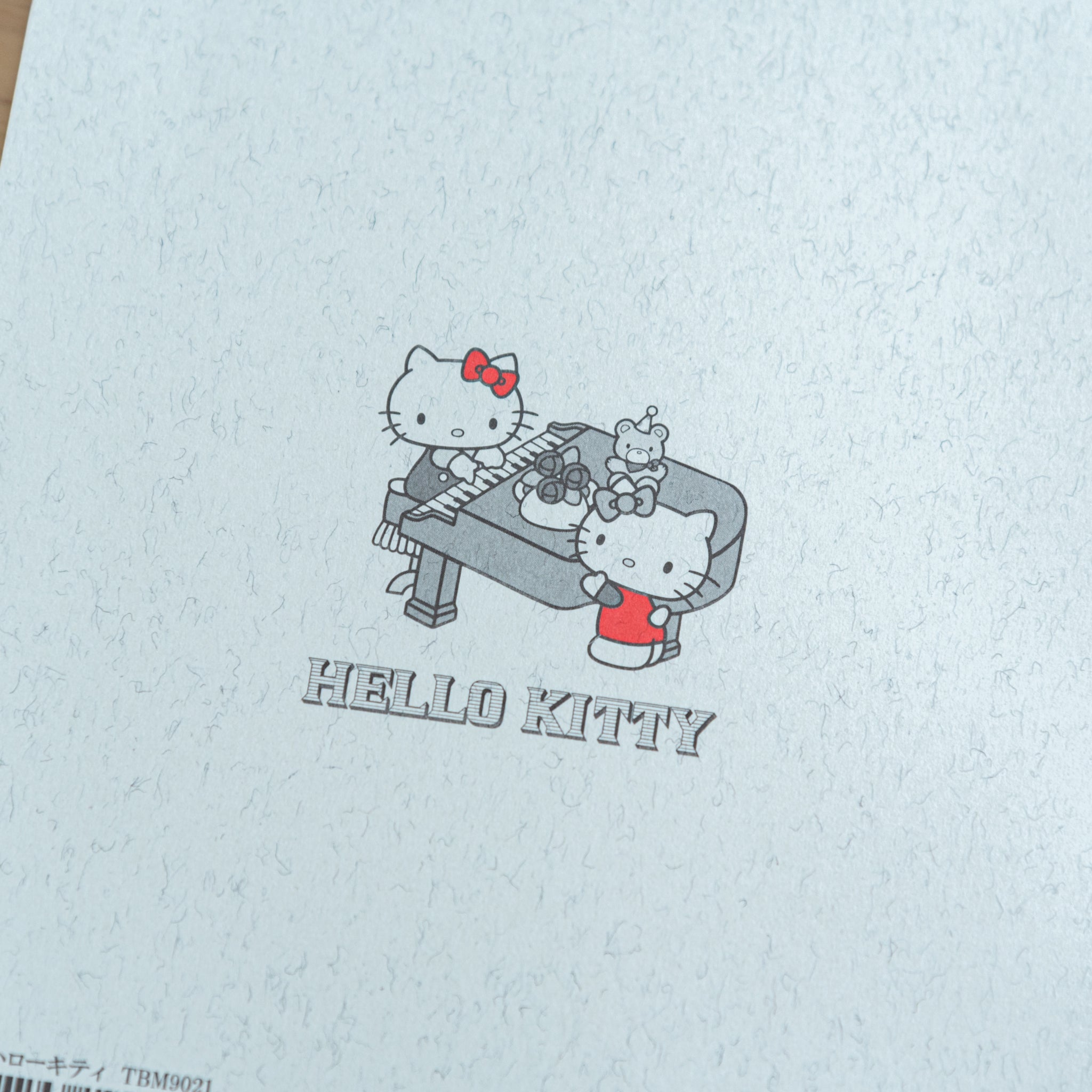 A close-up of the back cover of a Tsubame Japanese notebook, showing a Hello Kitty piano illustration with red accents, combining elegance with playful Japanese stationery.  