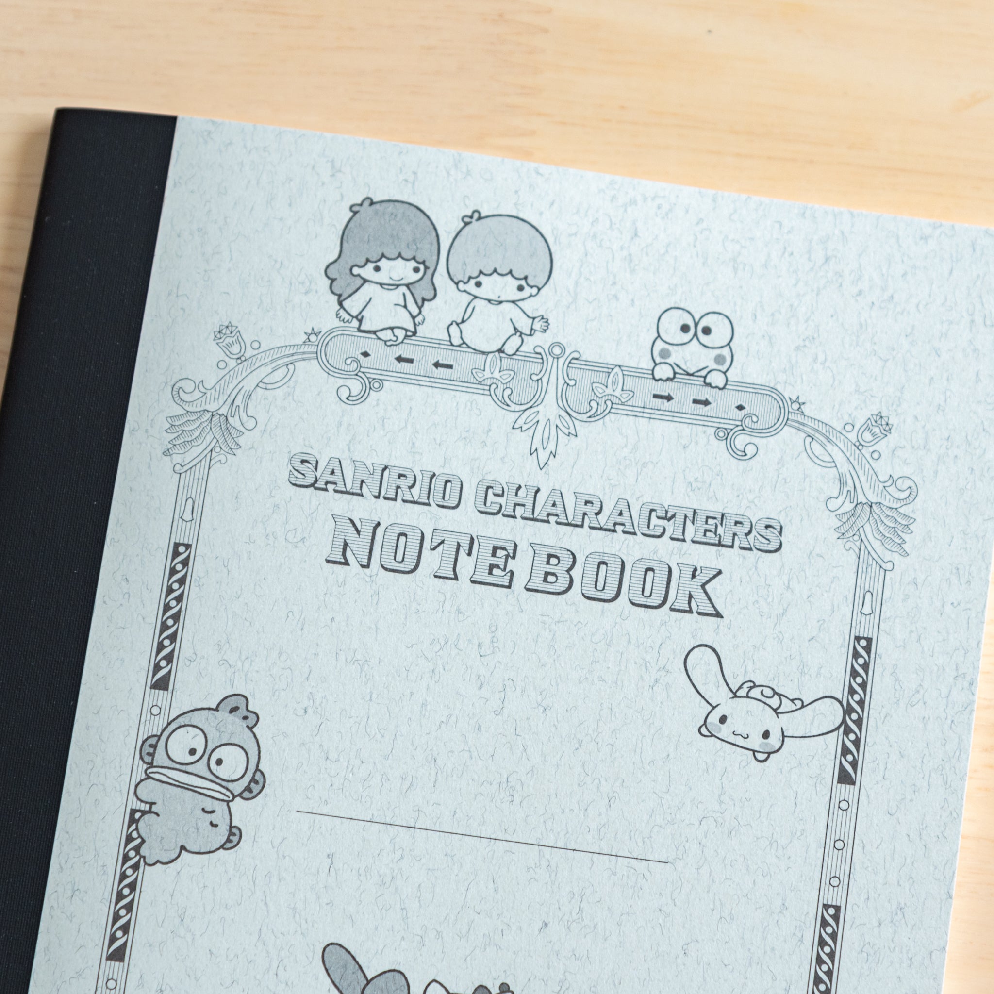 A close-up of a Japanese stationery notebook cover with Sanrio characters, including Hello Kitty and My Melody, drawn in a vintage-style decorative frame.  