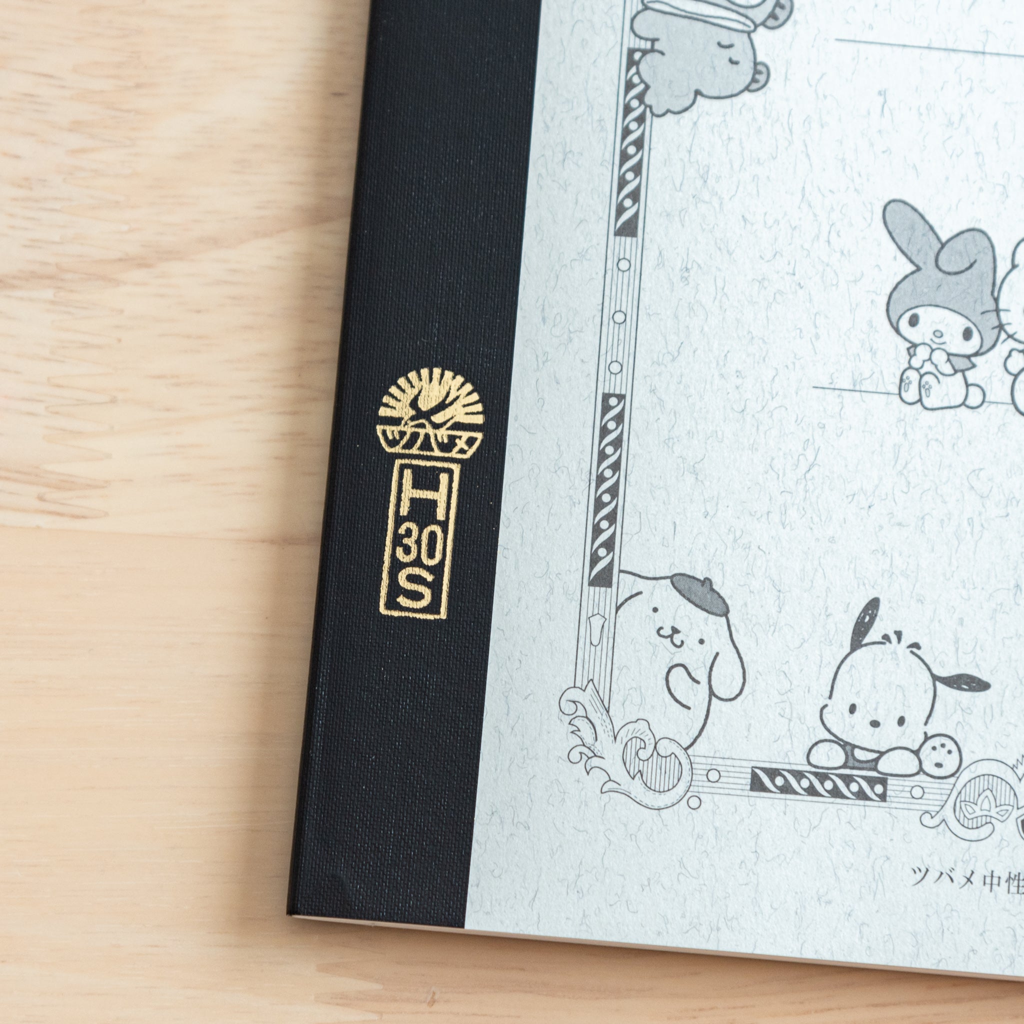 A close-up of a Tsubame Japanese notebook’s spine, featuring a gold-stamped logo and part of the Hello Kitty design with red accents, highlighting premium Japanese stationery.  