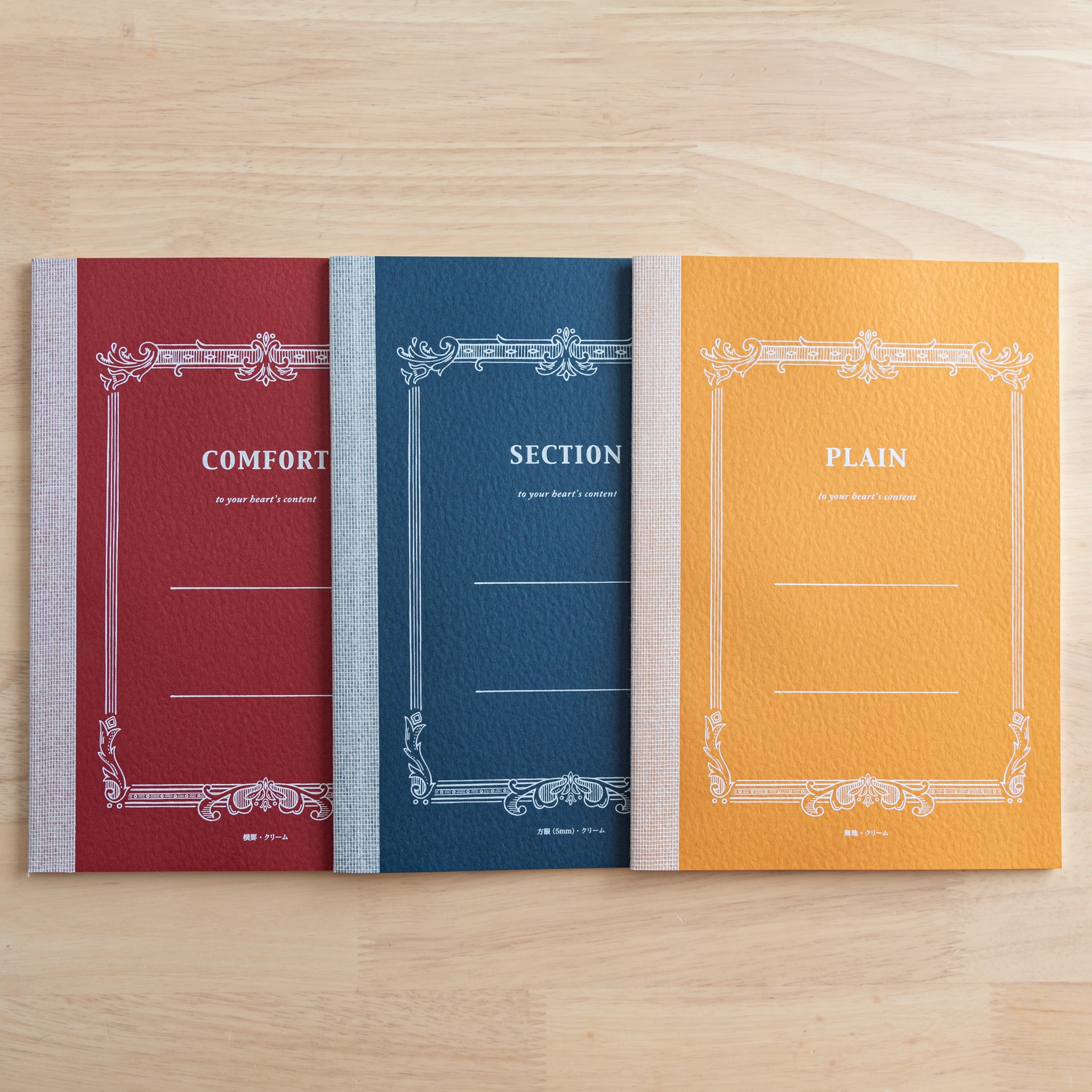 Three Tsubame Japanese notebooks on a wooden surface, labeled "Comfort," "Section," and "Plain," featuring elegant vintage-style covers. A classic piece of Japanese stationery.