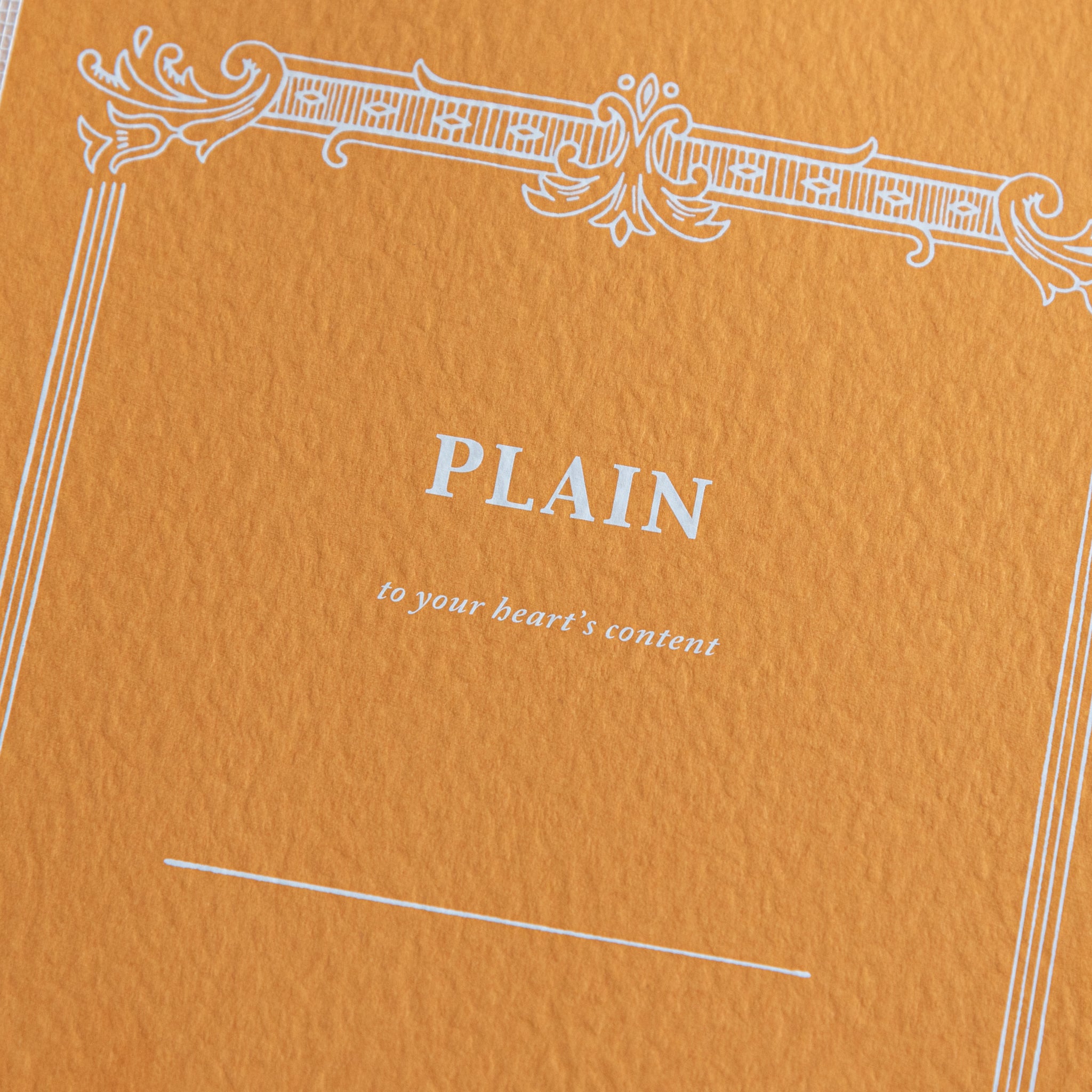 A close-up of the orange cover of a Tsubame Japanese notebook labeled "Plain," featuring an ornate vintage-style design. A classic piece of Japanese stationery.