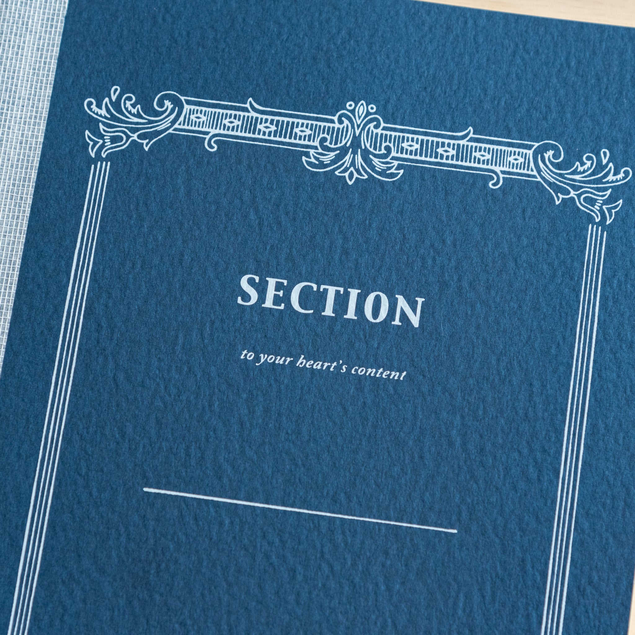 A close-up of the navy blue cover of a Tsubame Japanese notebook labeled "Section," featuring an ornate vintage-style design. A refined piece of Japanese stationery.