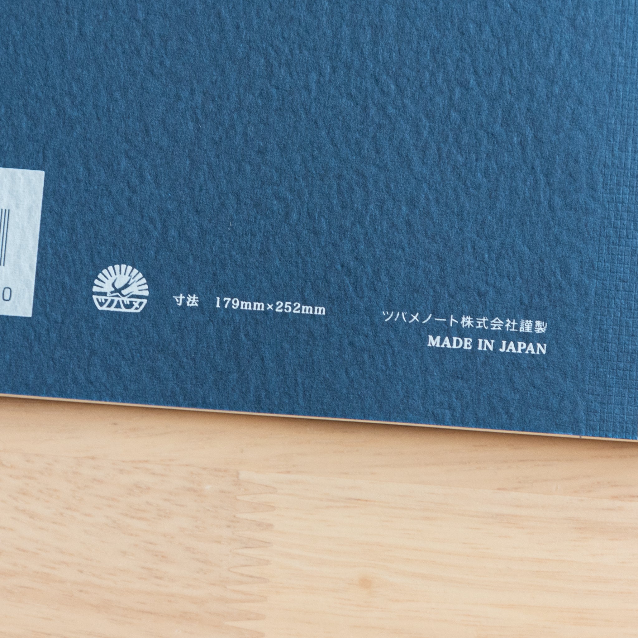 A close-up of the back cover of a Tsubame Japanese notebook, showing the logo, size details, and "Made in Japan" label on an orange textured surface.