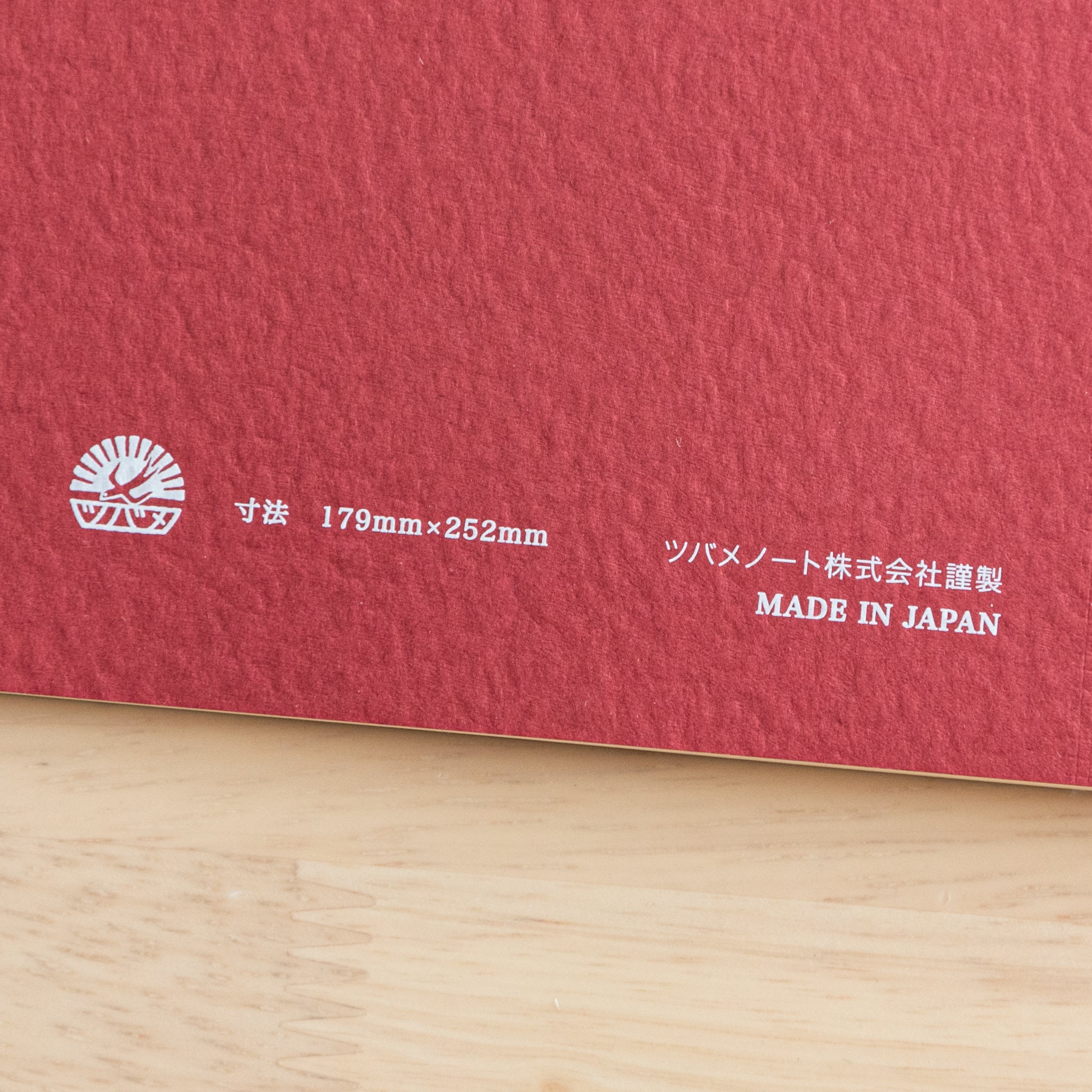 A close-up of the back cover of a Tsubame Japanese notebook, showing the logo, size details, and "Made in Japan" label on an orange textured surface.