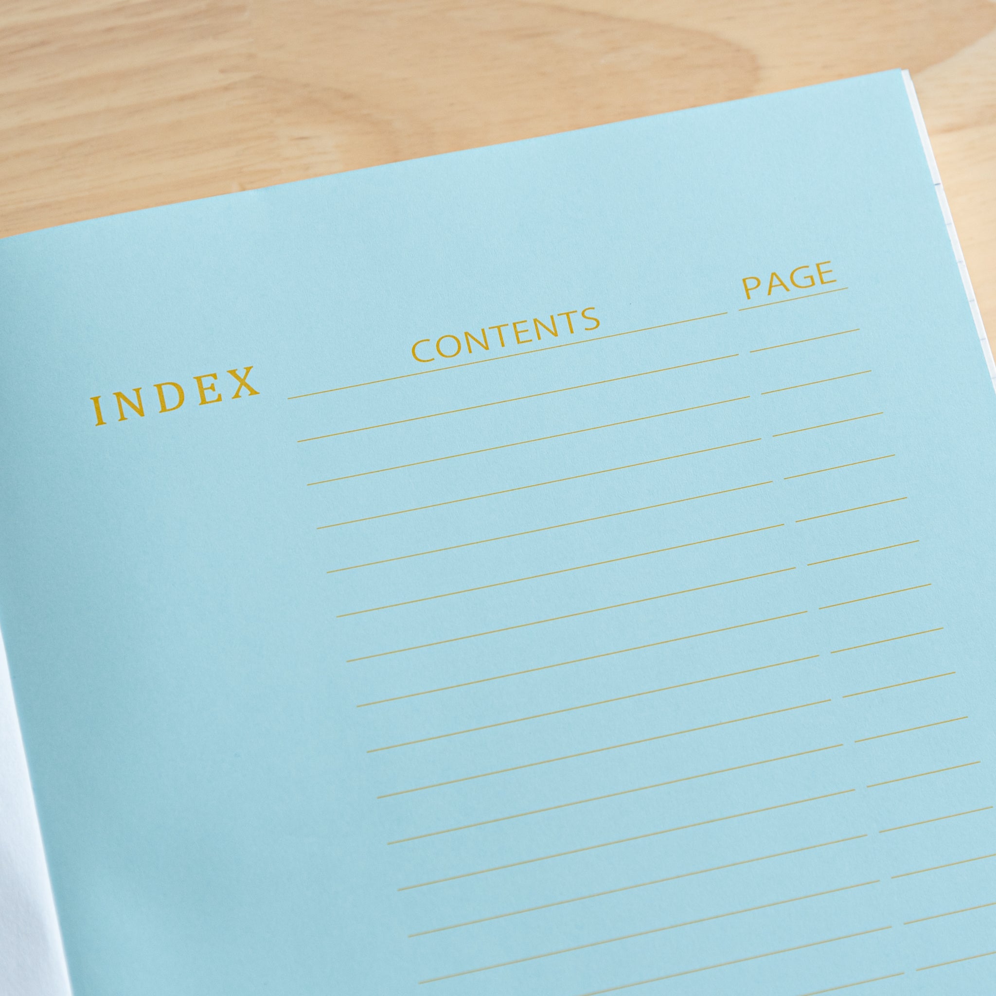 An open Japanese notebook displaying a light blue index page with gold lettering and a black ribbon bookmark, showcasing fine Japanese stationery.  