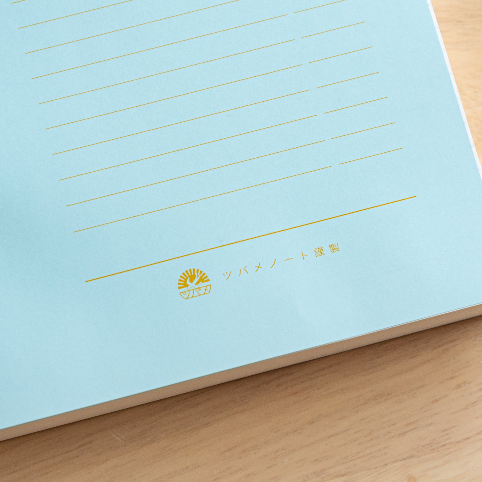 An open Japanese notebook displaying a light blue index page with gold lettering and a black ribbon bookmark, showcasing fine Japanese stationery.  