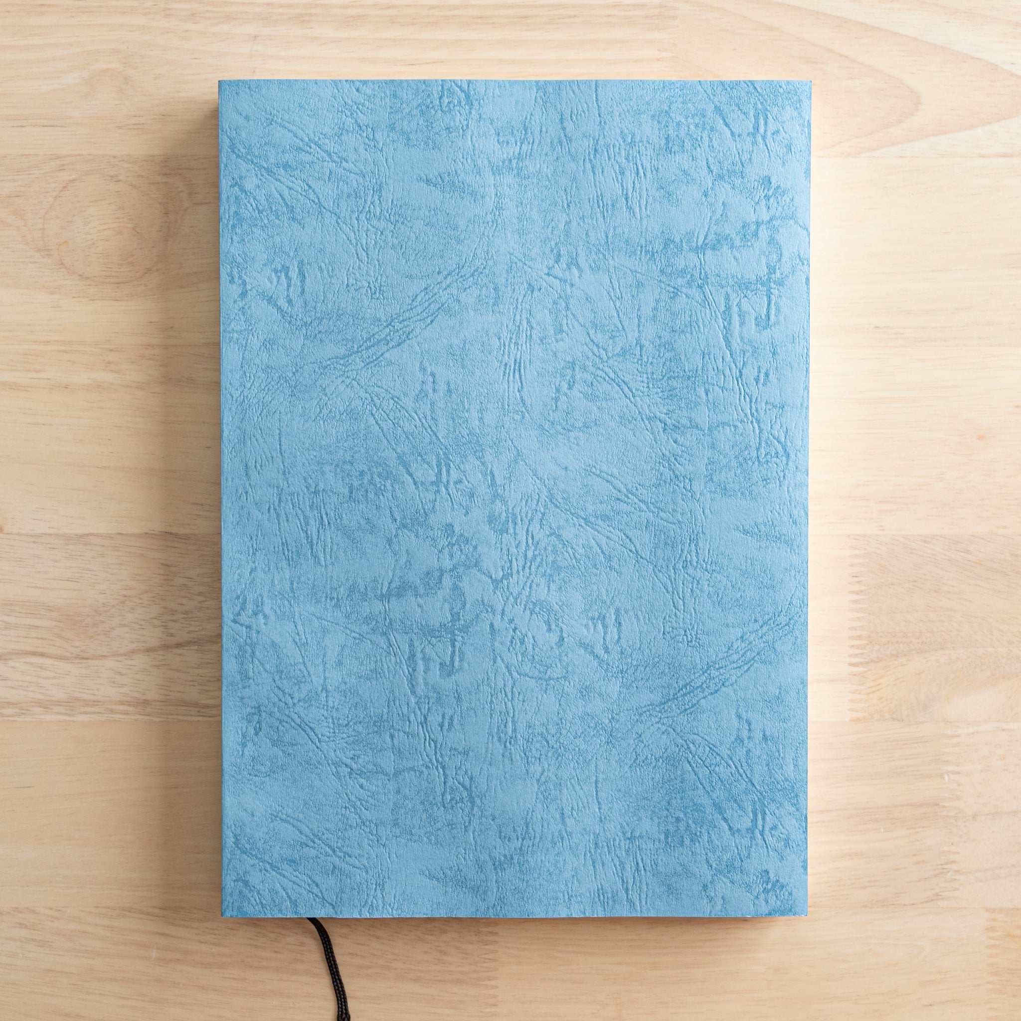 A Japanese notebook with a textured blue cover and a black ribbon bookmark, showcasing high-quality Japanese stationery with an elegant design.  