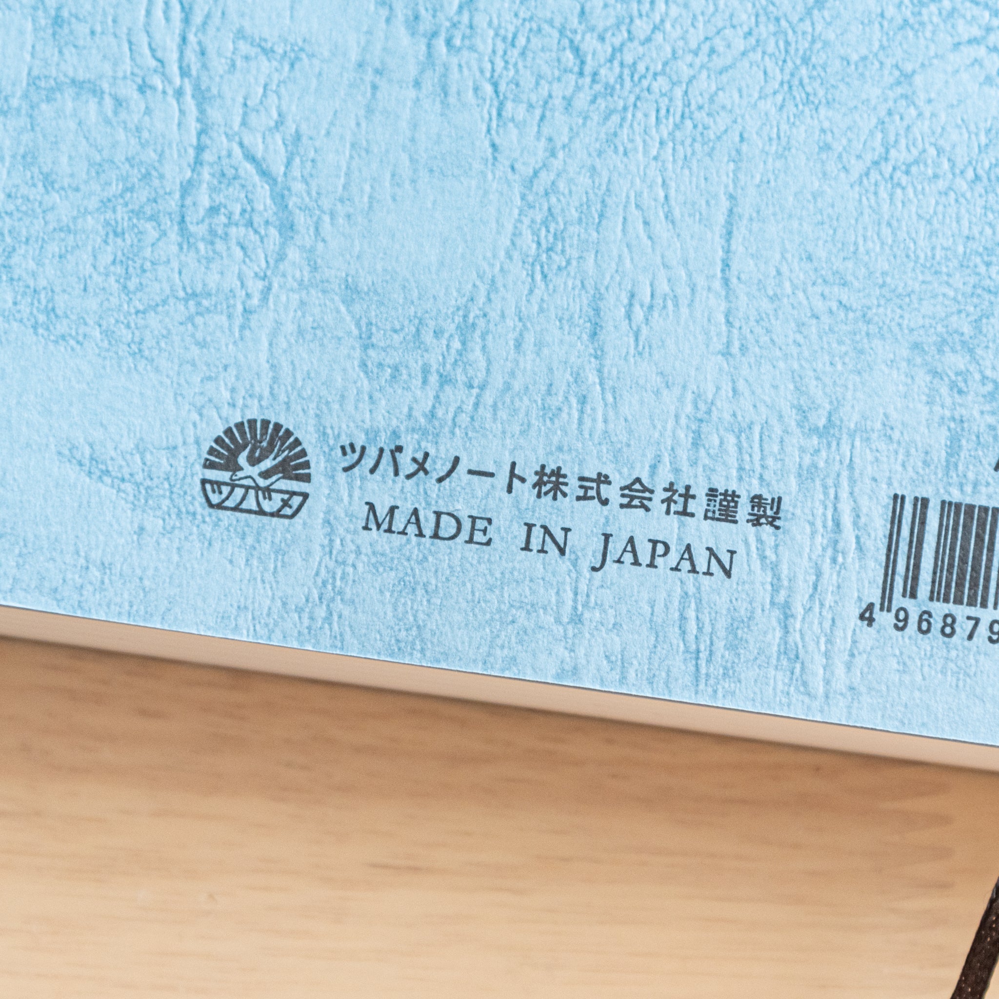 The back cover of a Japanese notebook with a textured blue design, featuring a barcode, brand logo, and "Made in Japan" text, representing fine Japanese stationery.  