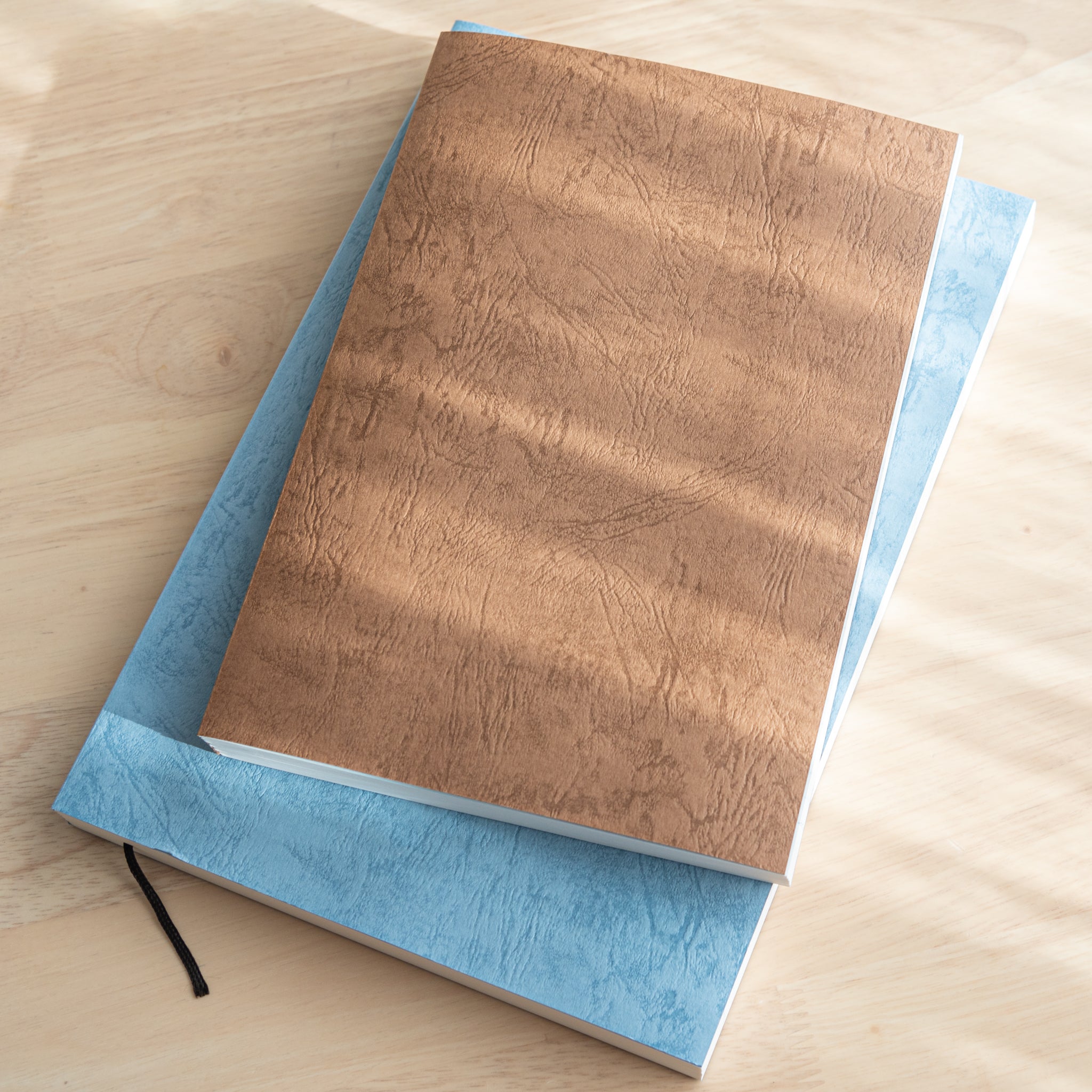 Two Japanese notebooks with textured covers, one brown and one blue, stacked. High-quality Japanese stationery with thick pages and stitched binding.  