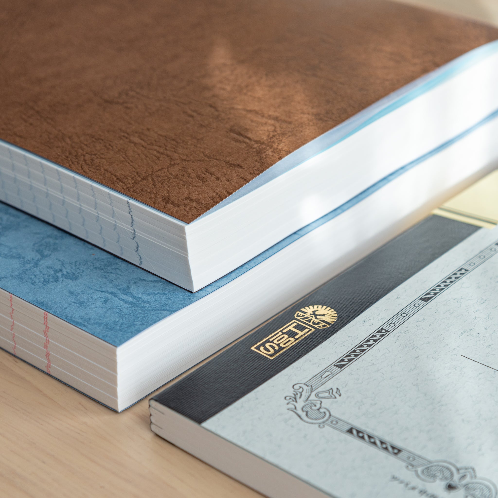 A close-up of Japanese stationery featuring stacked notebooks with textured covers, stitched bindings, and high-quality paper edges.  