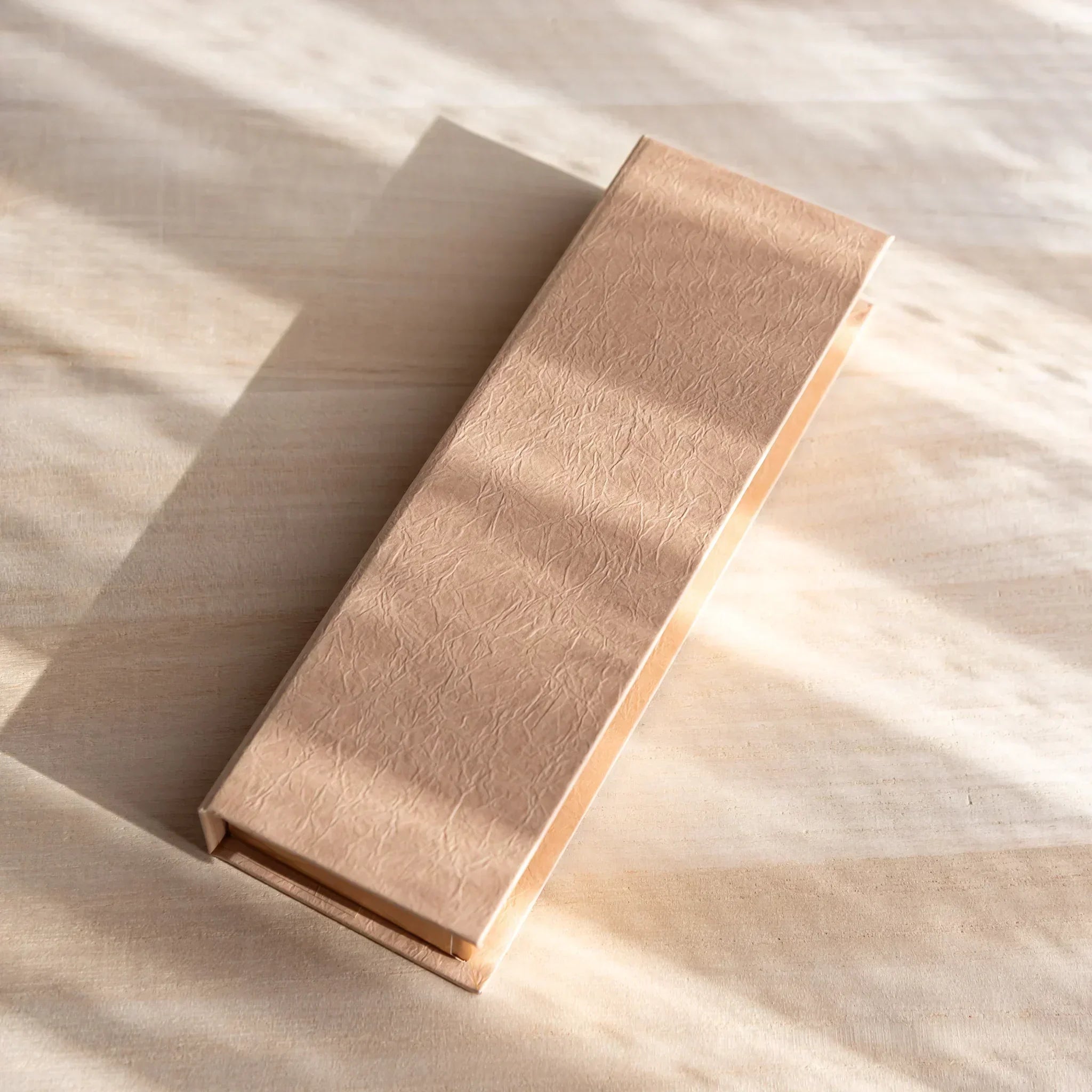 Gift box for the Gold Leaf Ballpoint Pen made of textured beige paper, softly lit by natural sunlight.