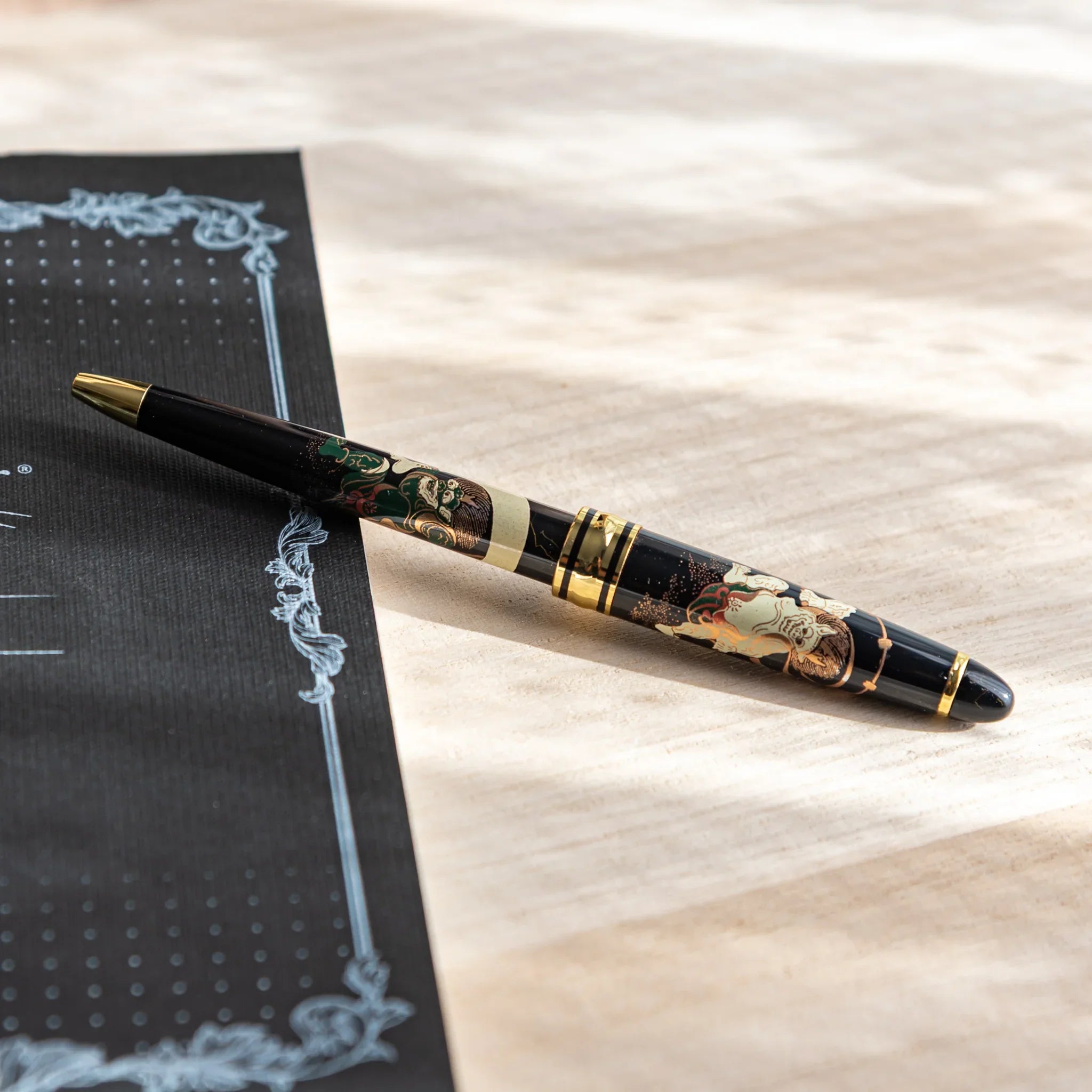 Japanese Ballpoint Pen with gold and black Raijin and Fujin design resting on the desk.