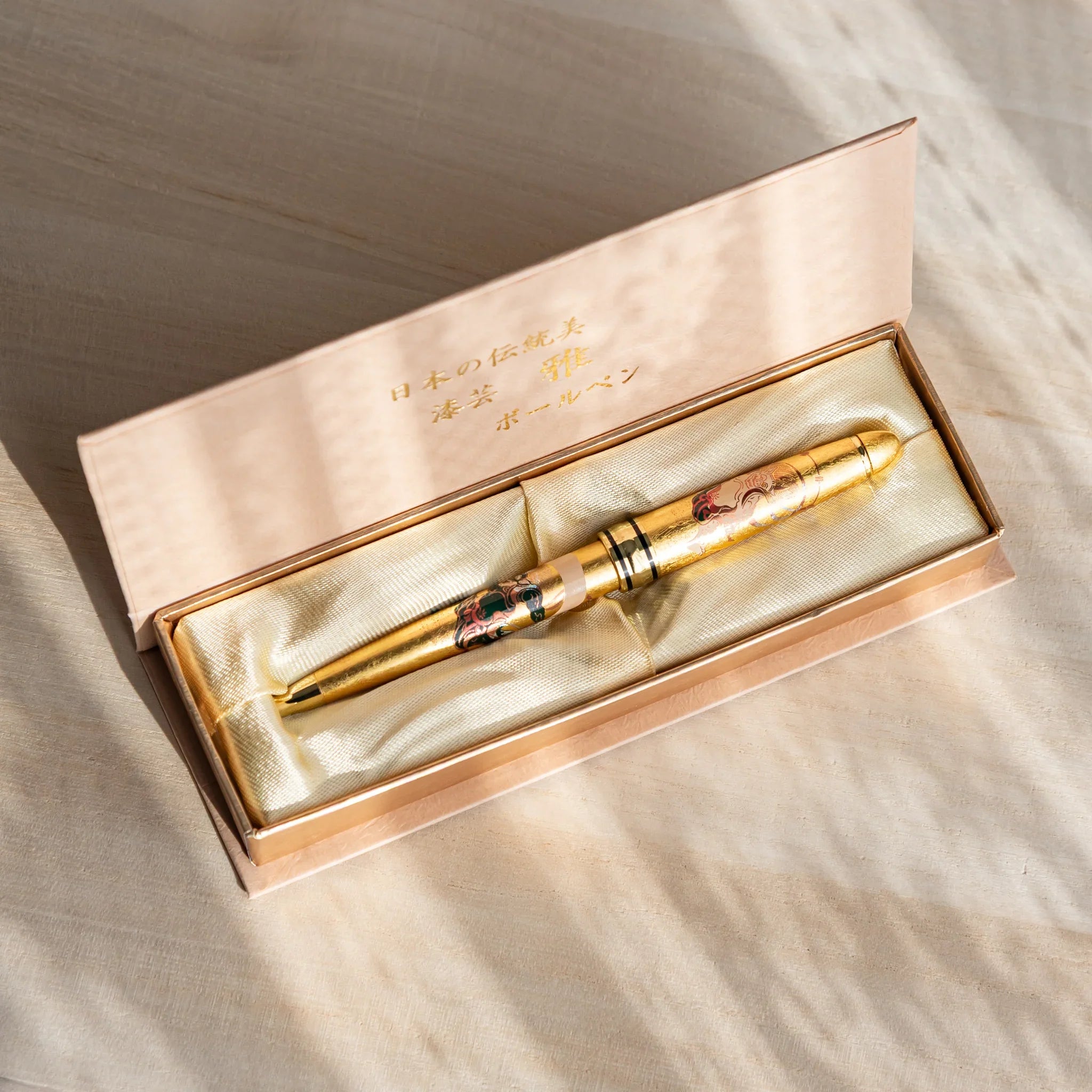Gold leaf Japanese Ballpoint Pen in a satin-lined gift box, showing Raijin and Fujin artwork under warm light.