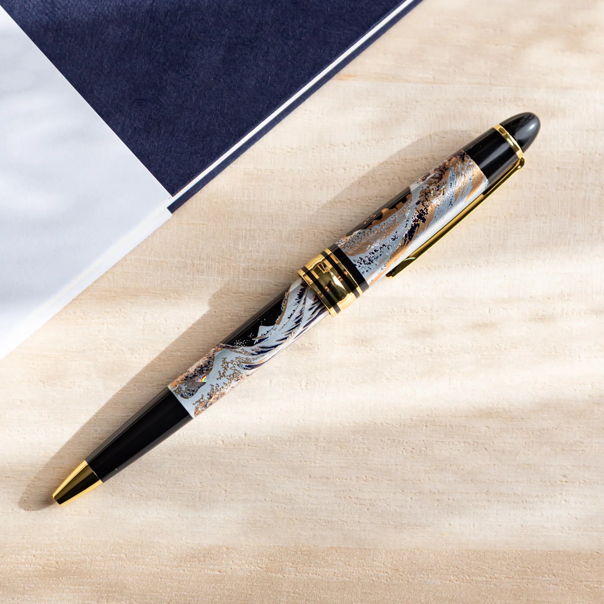 Japanese Ballpoint Pen with a navy notebook, displaying the detailed blue Great Wave pattern and gold decorative rings.